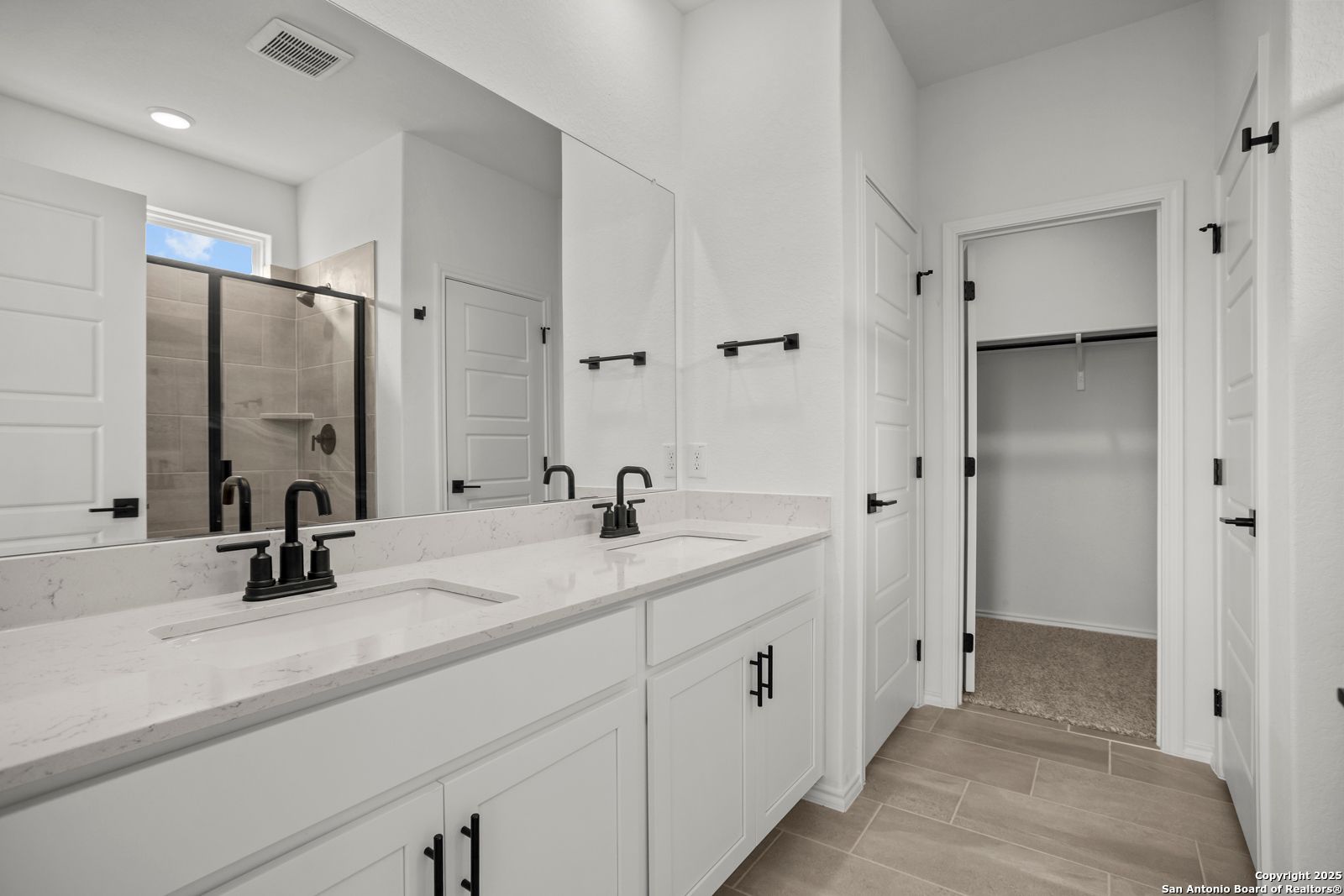 Modern master bathroom featuring double vanity with quartz countertop, glass walk-in shower, and adjacent closet in Davidson Homes The Daphne K, San Antonio