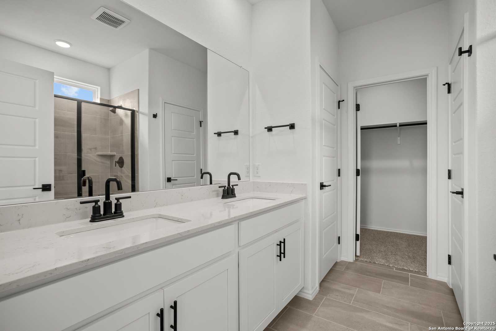 Modern master bathroom featuring double vanity with quartz countertop, glass walk-in shower, and adjacent closet in Davidson Homes The Daphne K, San Antonio
