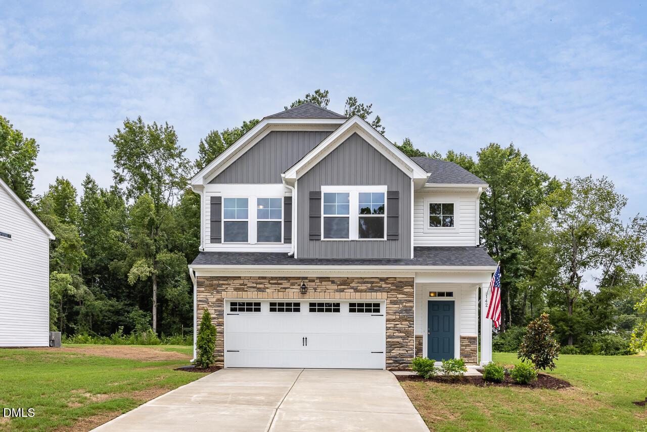 Two-story gray home with stone garage, blue door, and American flag in Retreat at North Main, Lillington, NC - Davidson Homes Grace C