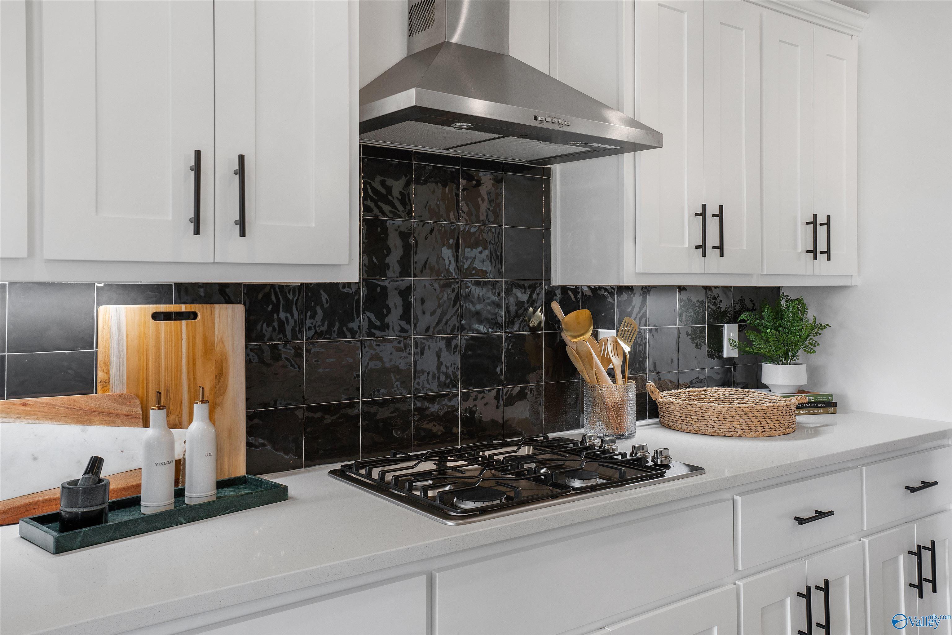 Modern kitchen featuring white cabinets, black subway tile backsplash, stainless gas range in Davidson Homes The Rockford B, Madison, Alabama