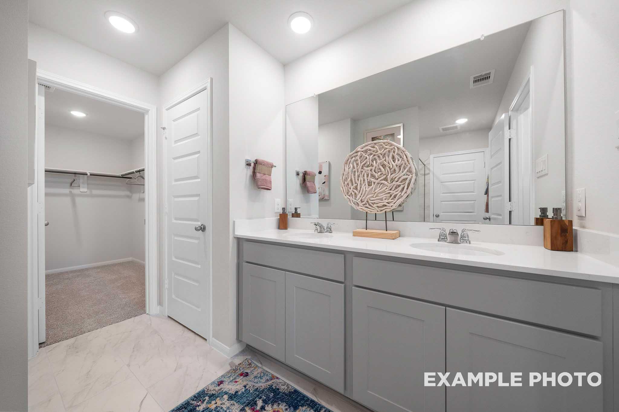 Spacious master bathroom in The Trinity E with double gray vanity, large mirror, and adjacent walk-in closet