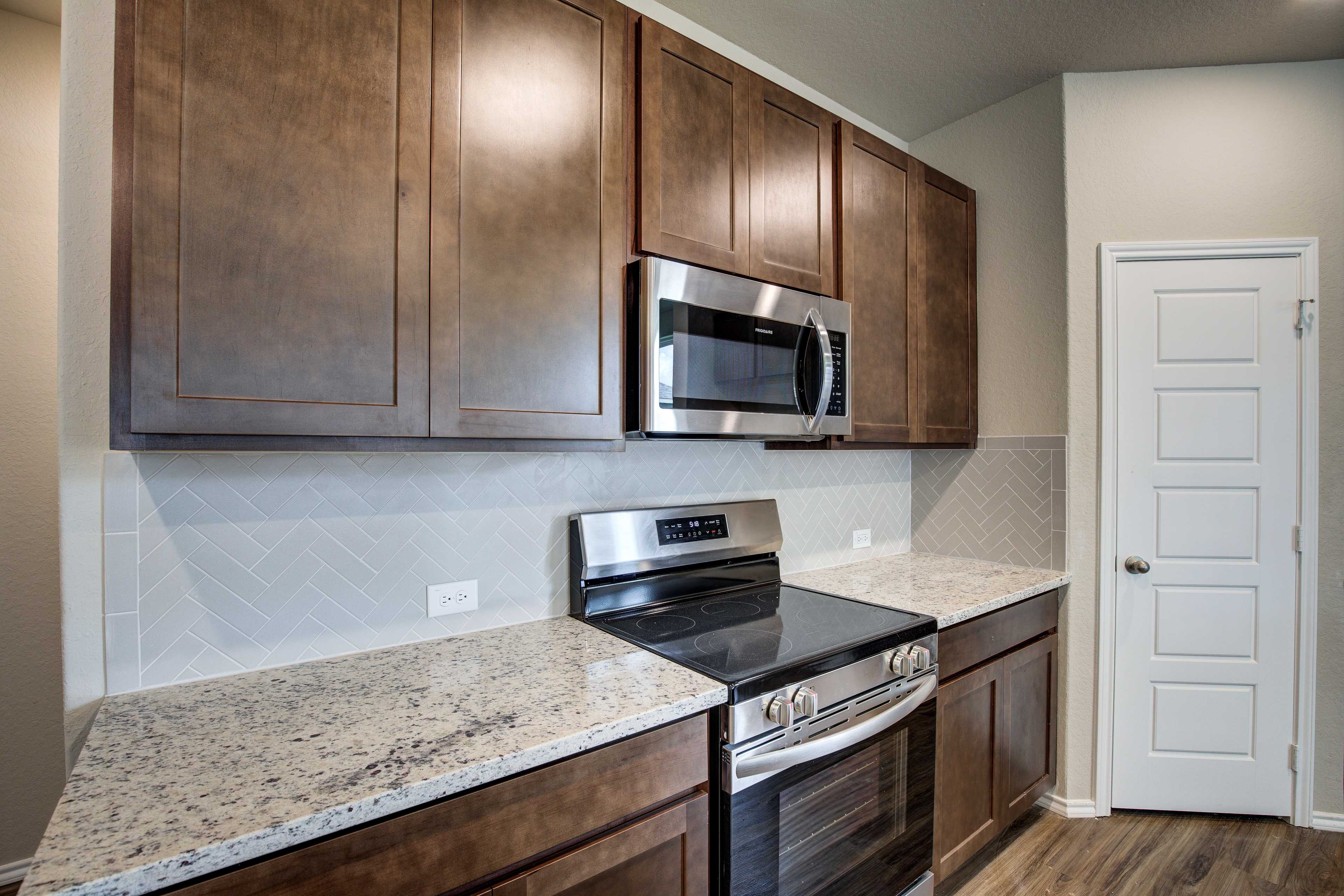 Spacious kitchen in The Murray with warm shaker cabinets, herringbone tile backsplash, granite counters, stainless steel appliances