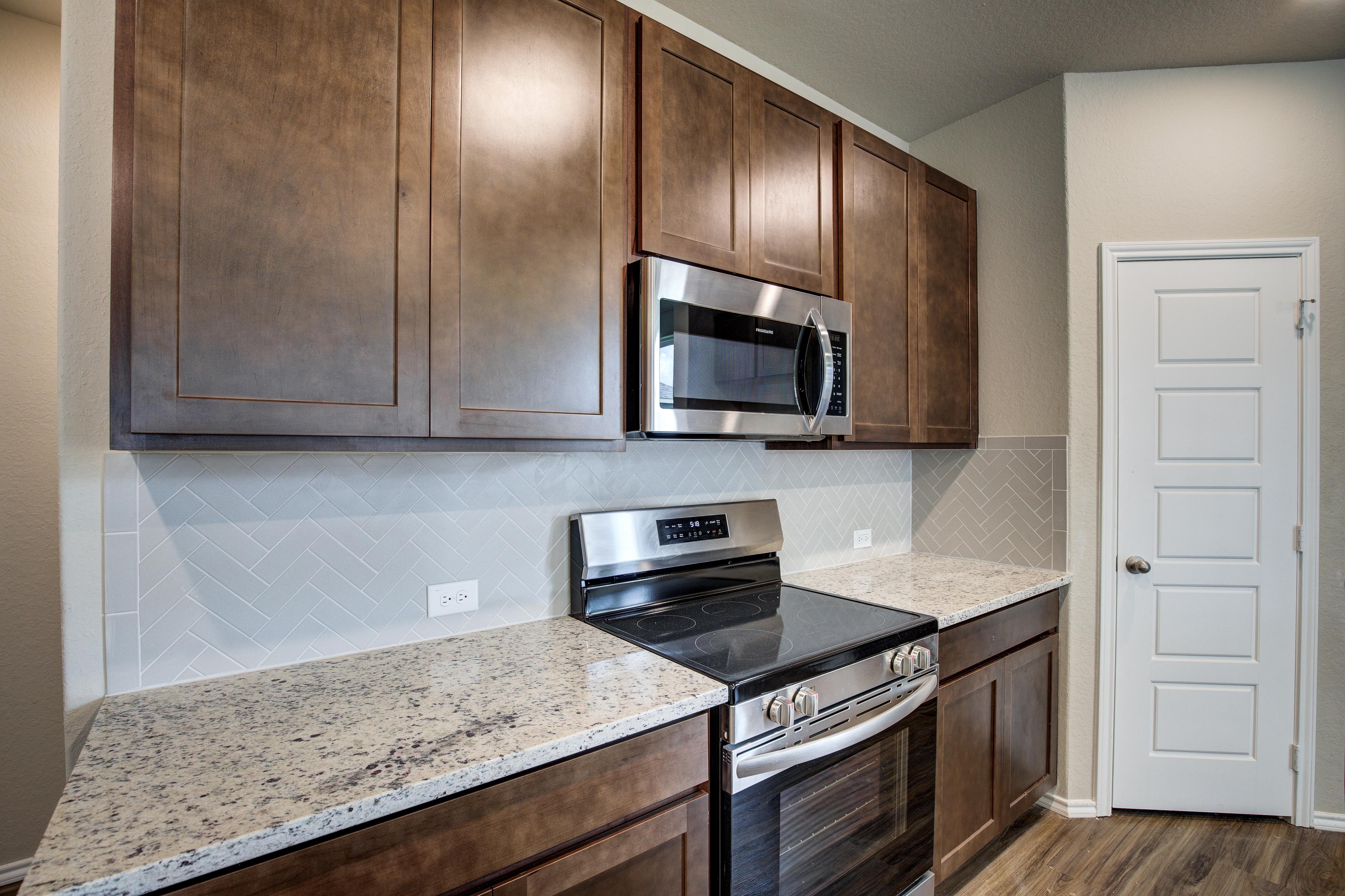 The Murray G kitchen featuring warm shaker cabinets, stainless steel appliances, herringbone backsplash, quartz counters