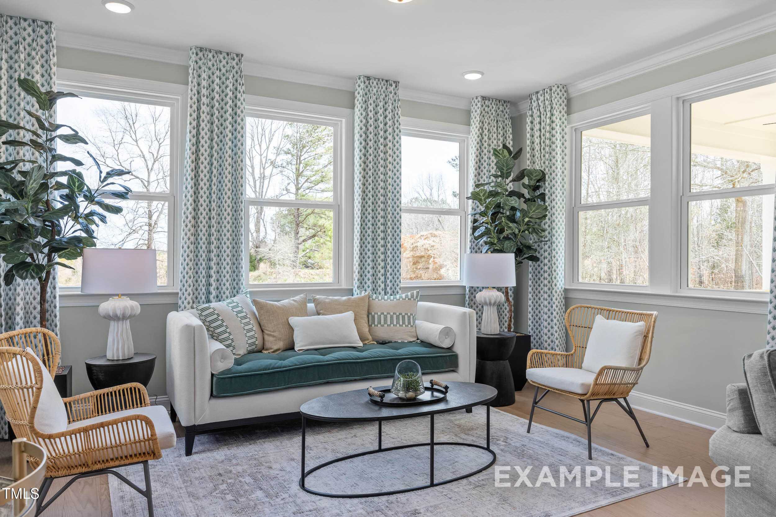 Bright living room with green velvet sofa, wicker chairs, potted plants, and large curtained windows in Davidson Homes Crawford B, Raleigh, NC