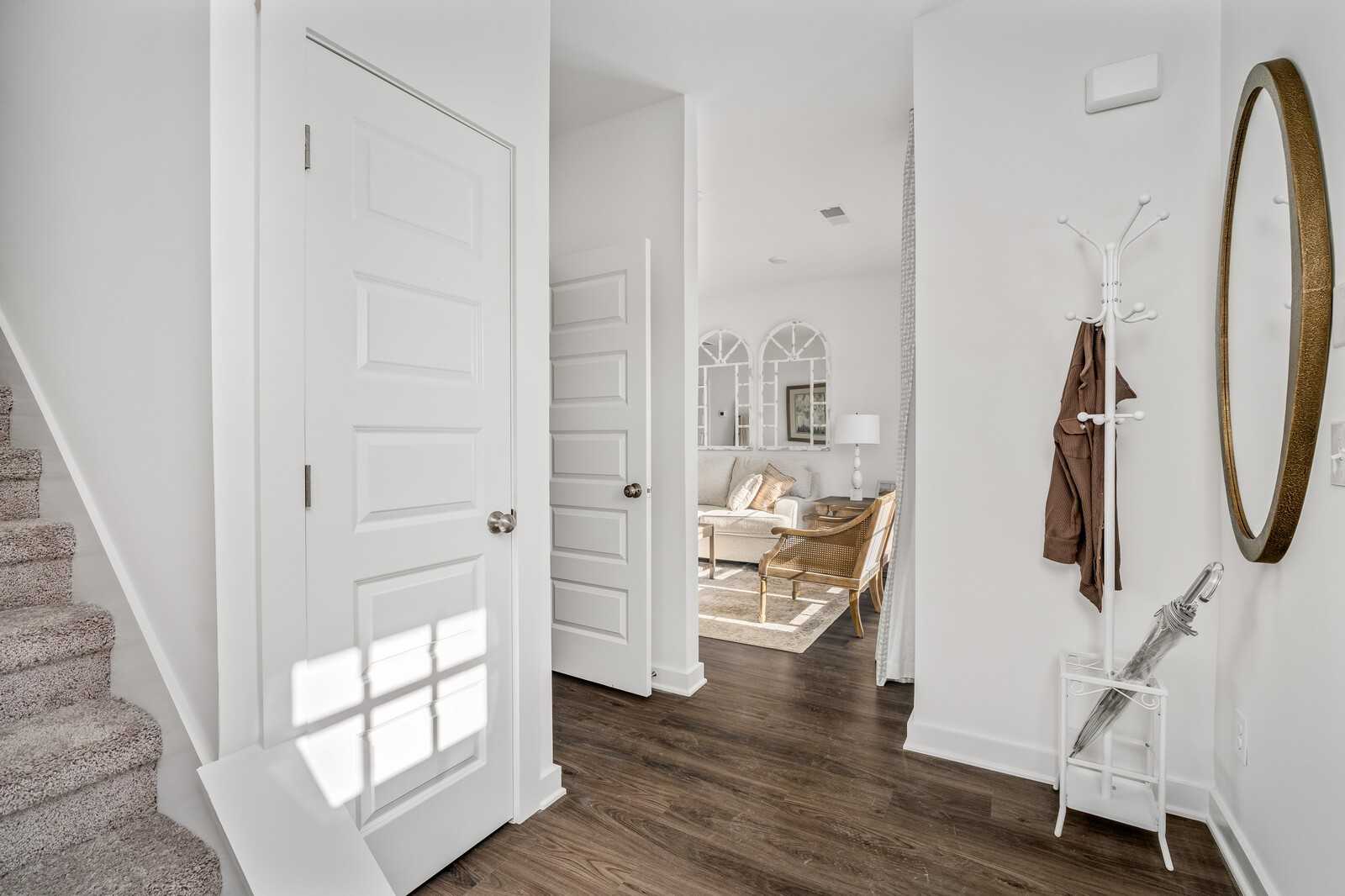 Bright foyer with hardwood floors, open white doors, coat rack, round mirror, and glimpse of living room in Davidson Homes The Cumberland A, Gallatin, TN