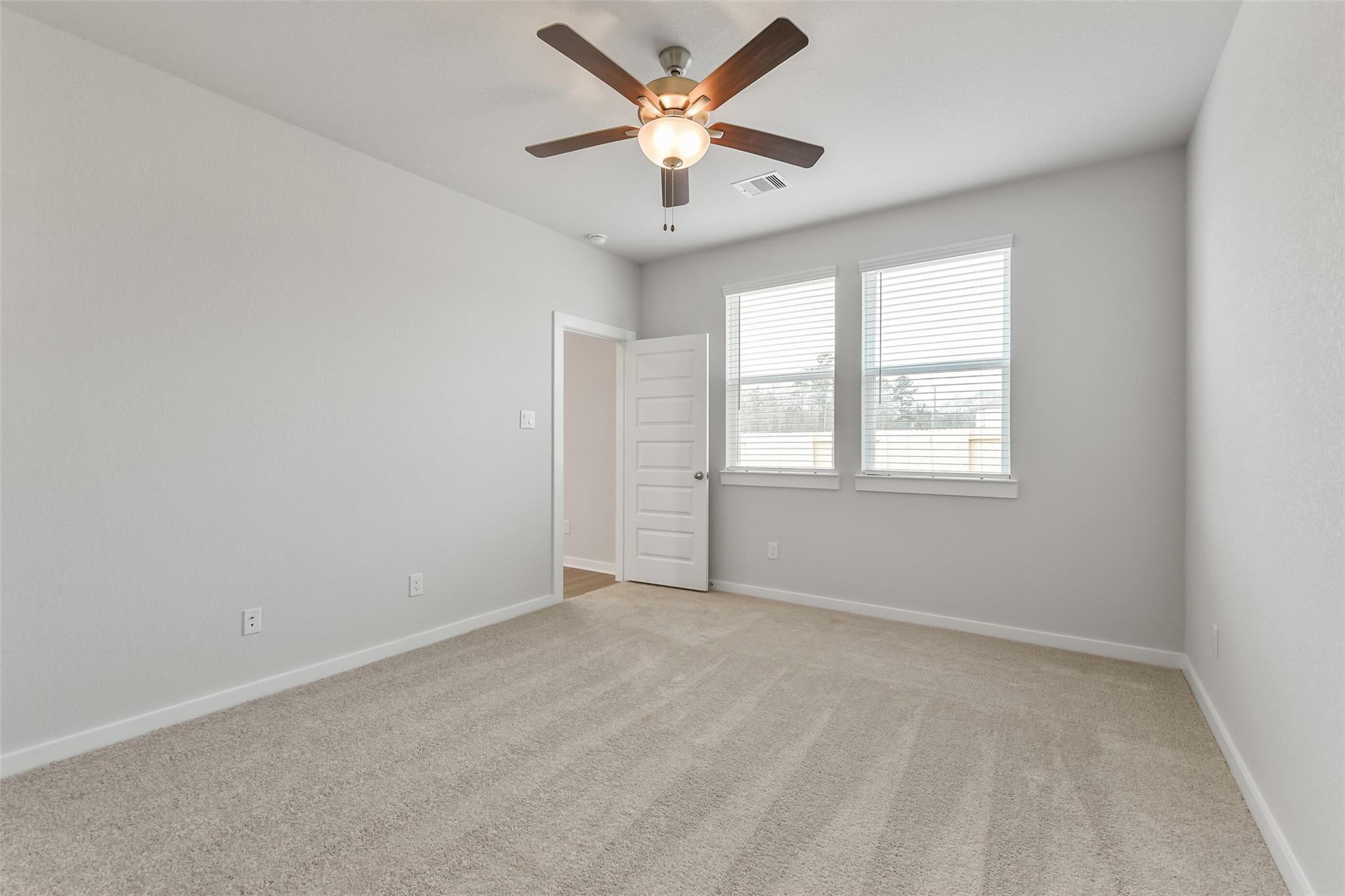Spacious bedroom with ceiling fan, large windows, plush carpet, and neutral walls in Davidson Homes The Brazos E, Cleveland, Texas