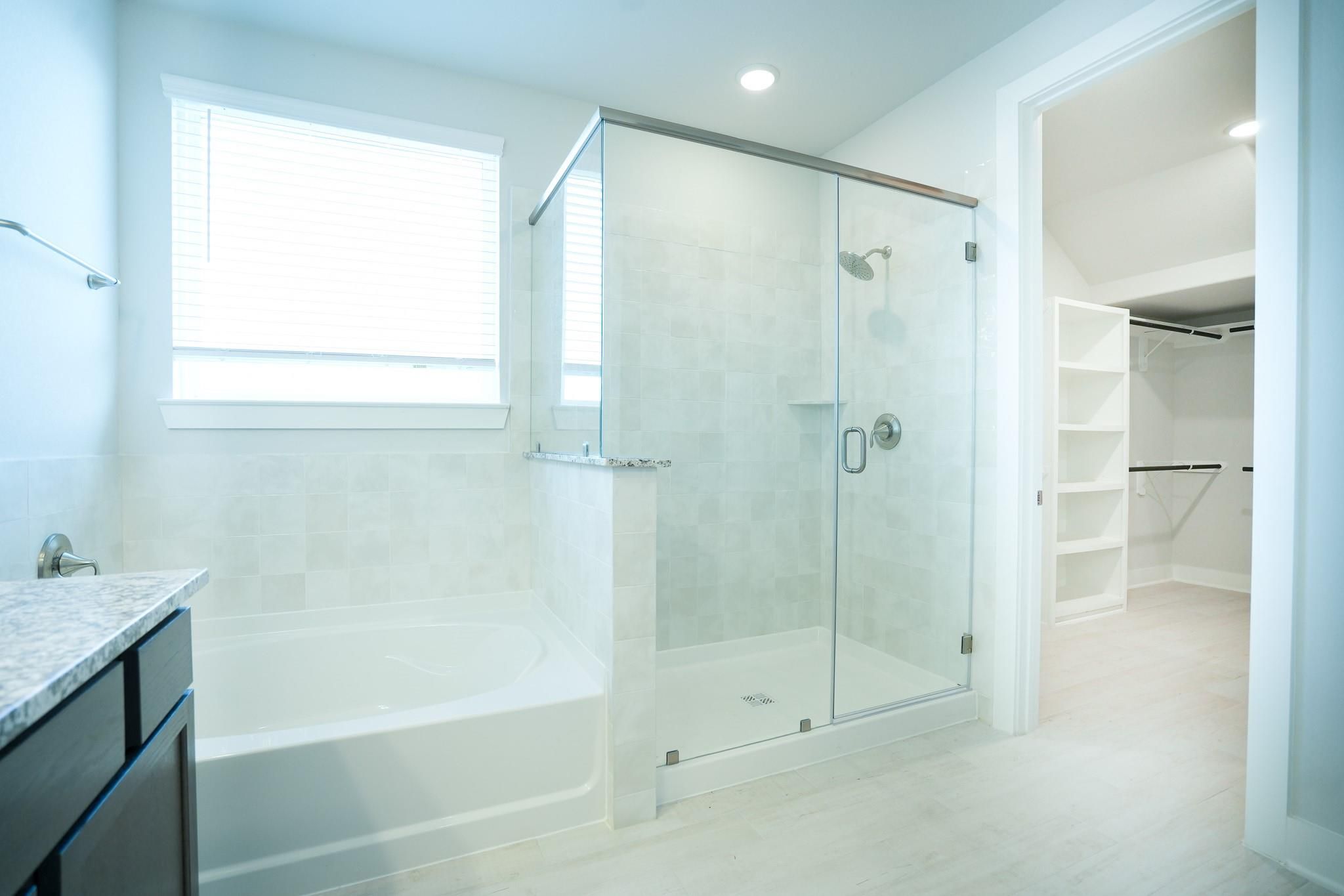 Modern master bathroom with frameless glass shower, soaking tub, granite vanity, and adjacent walk-in closet in Davidson Homes The Edward C, Lago Mar, Texas City