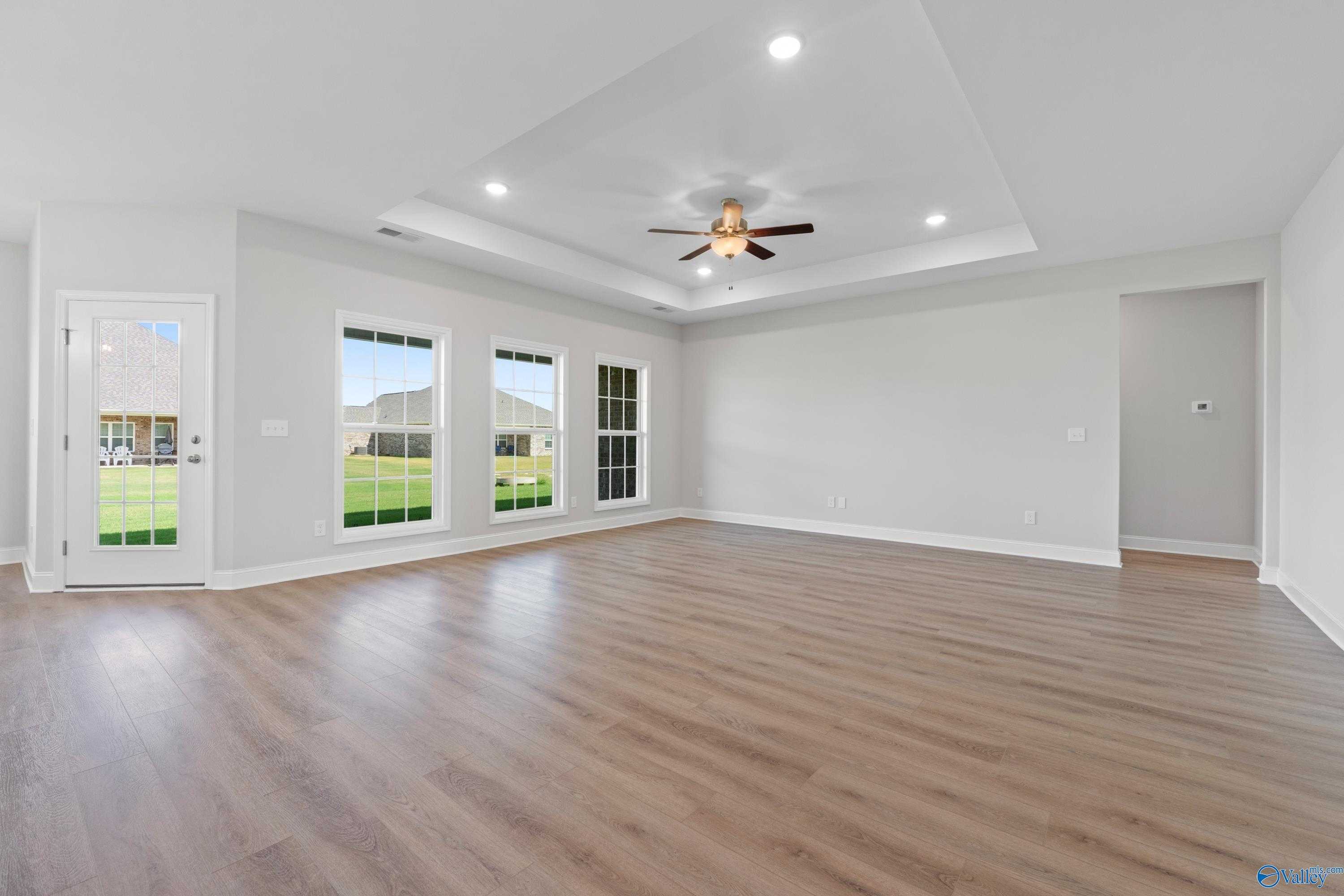 Bright living room with hardwood floors, ceiling fan, recessed lights, and large windows overlooking green yard in The Harrison B home by Davidson Homes, Meridianville, Alabama