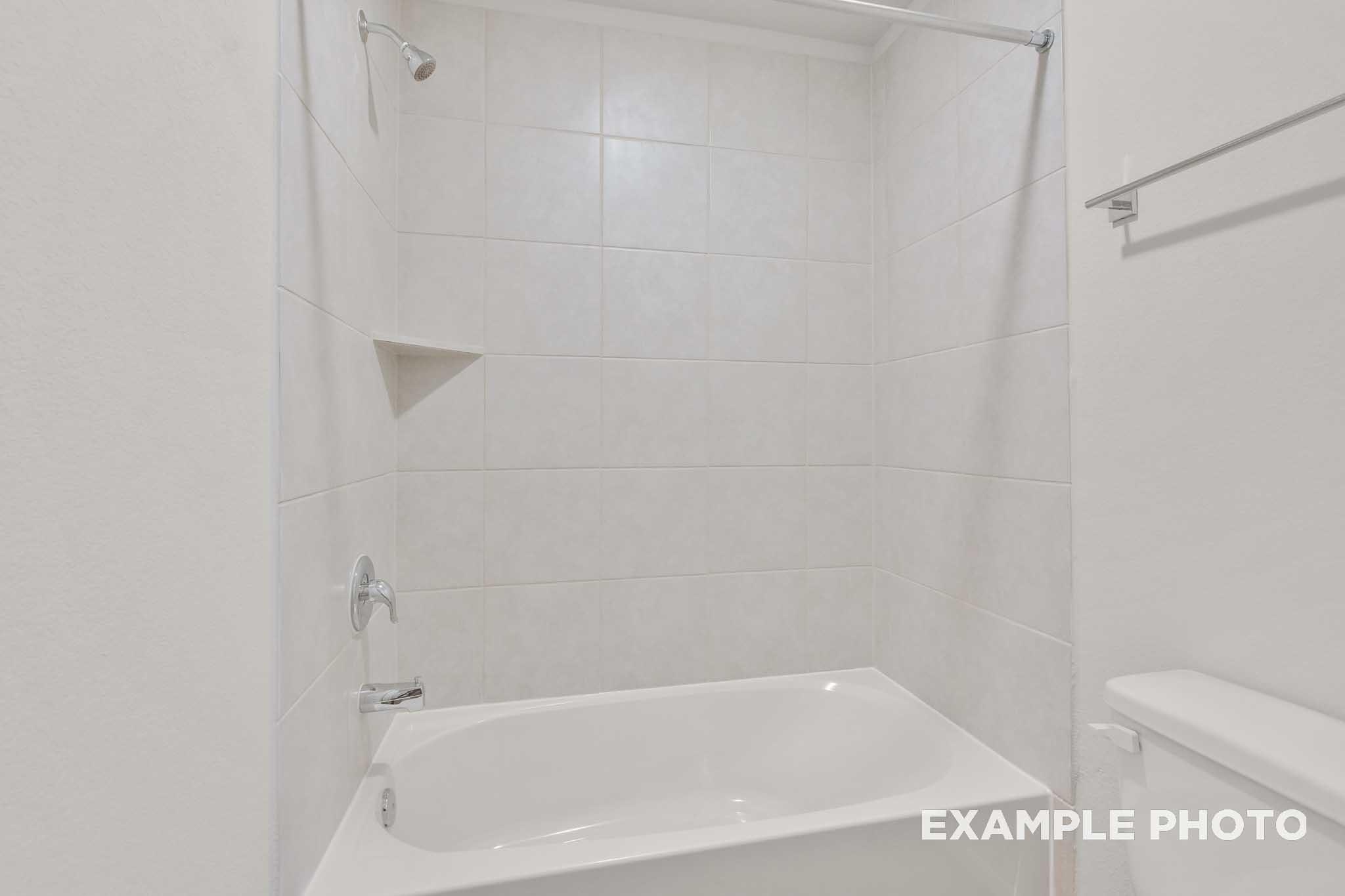 White tile shower and bathtub in the bathroom of The Brazos, a Davidson Homes single-family design in Beasley, Texas.