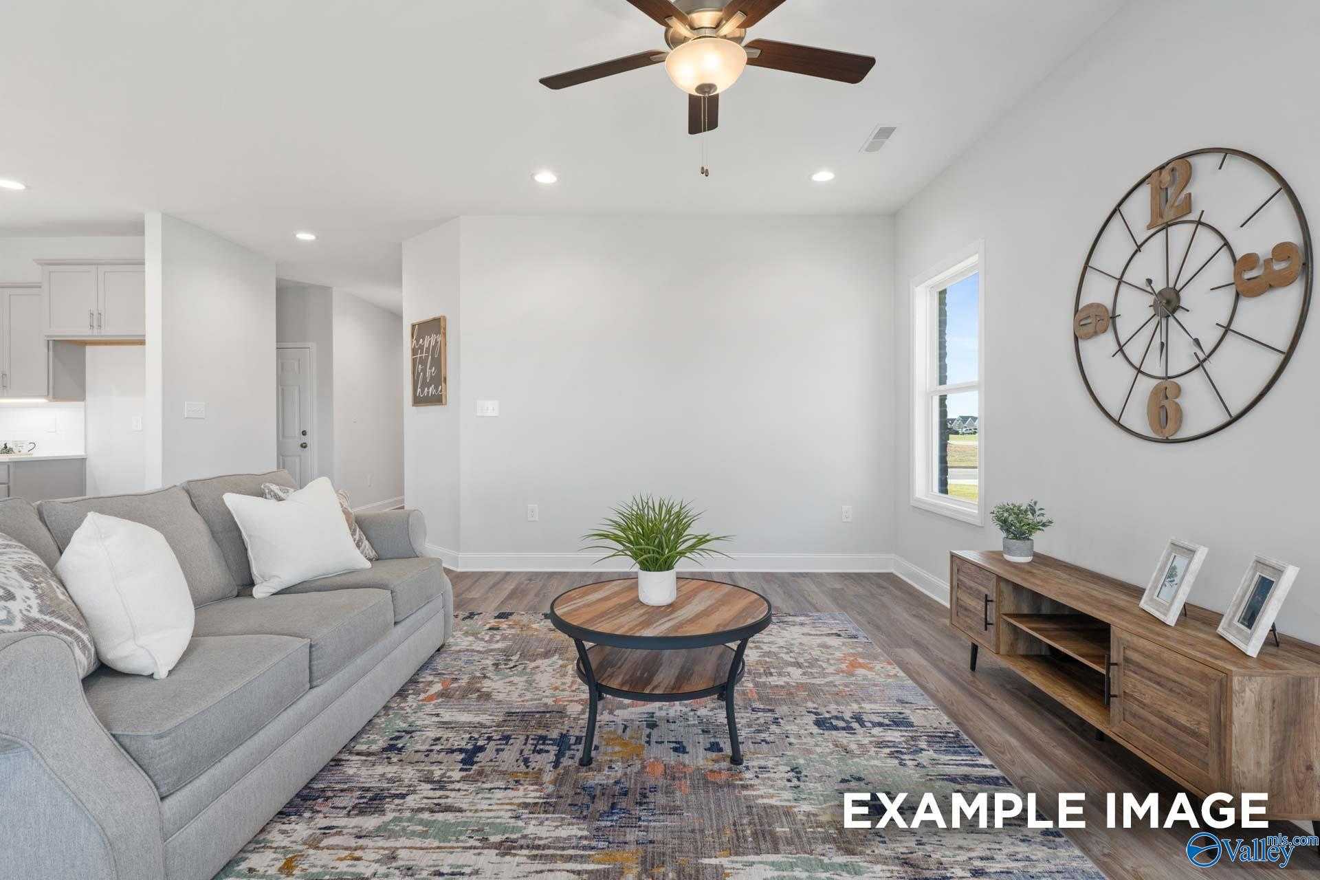 Cozy living room with gray sofa, rustic wall clock, ceiling fan, and plants in Davidson Homes The Franklin C, Meridianville, Alabama