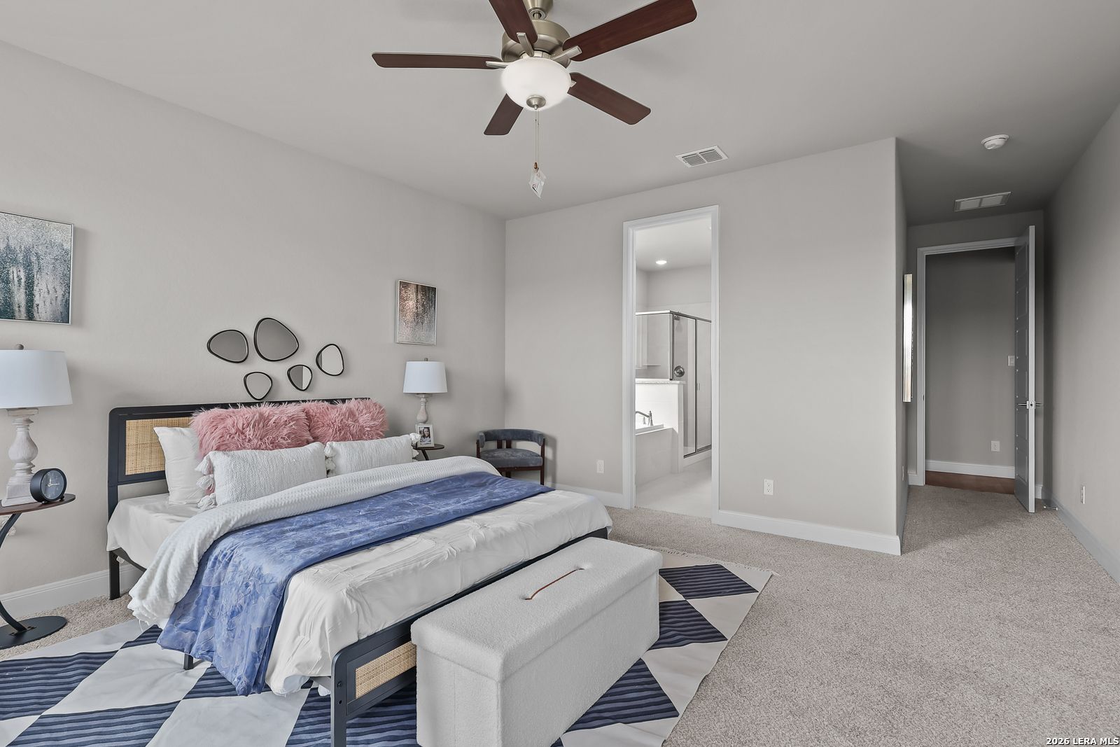 Elegant master bedroom with king bed, pink pillows, ceiling fan, and ensuite shower in Davidson Homes The Rockford G, Ladera, San Antonio