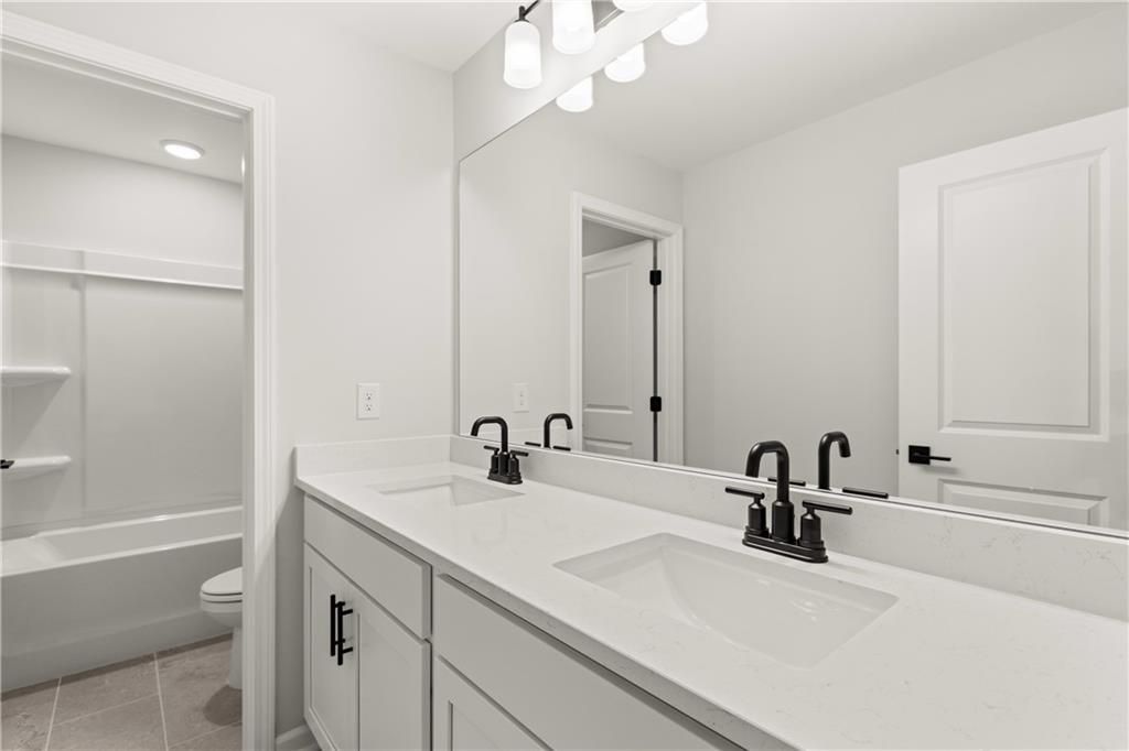 Modern master bathroom featuring double white quartz vanity, black faucets, and adjacent tub in Davidson Homes The Hickory B, Winder, Georgia