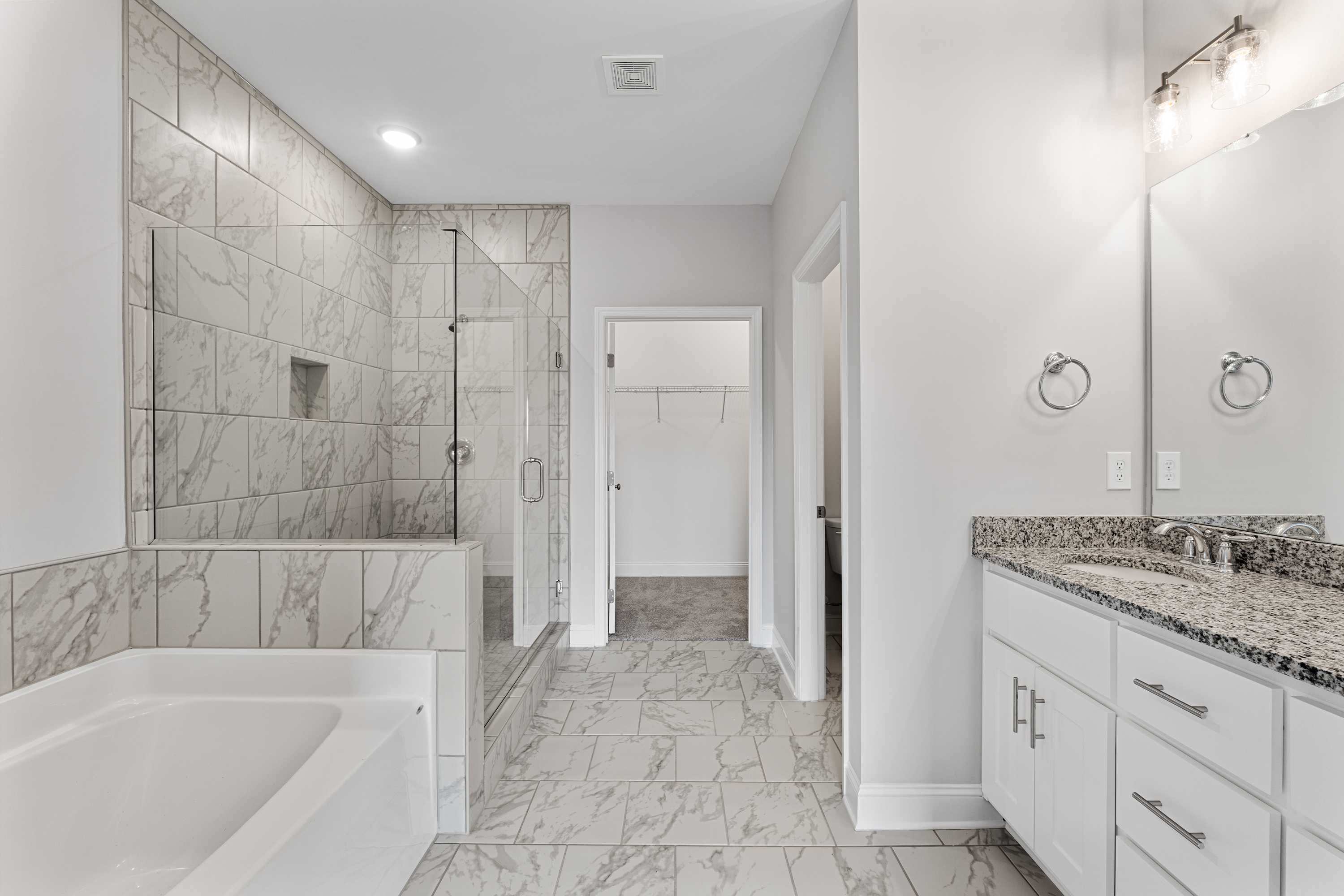 Luxurious master bathroom in The Copeland B featuring marble tile, freestanding tub, glass shower, and double vanity