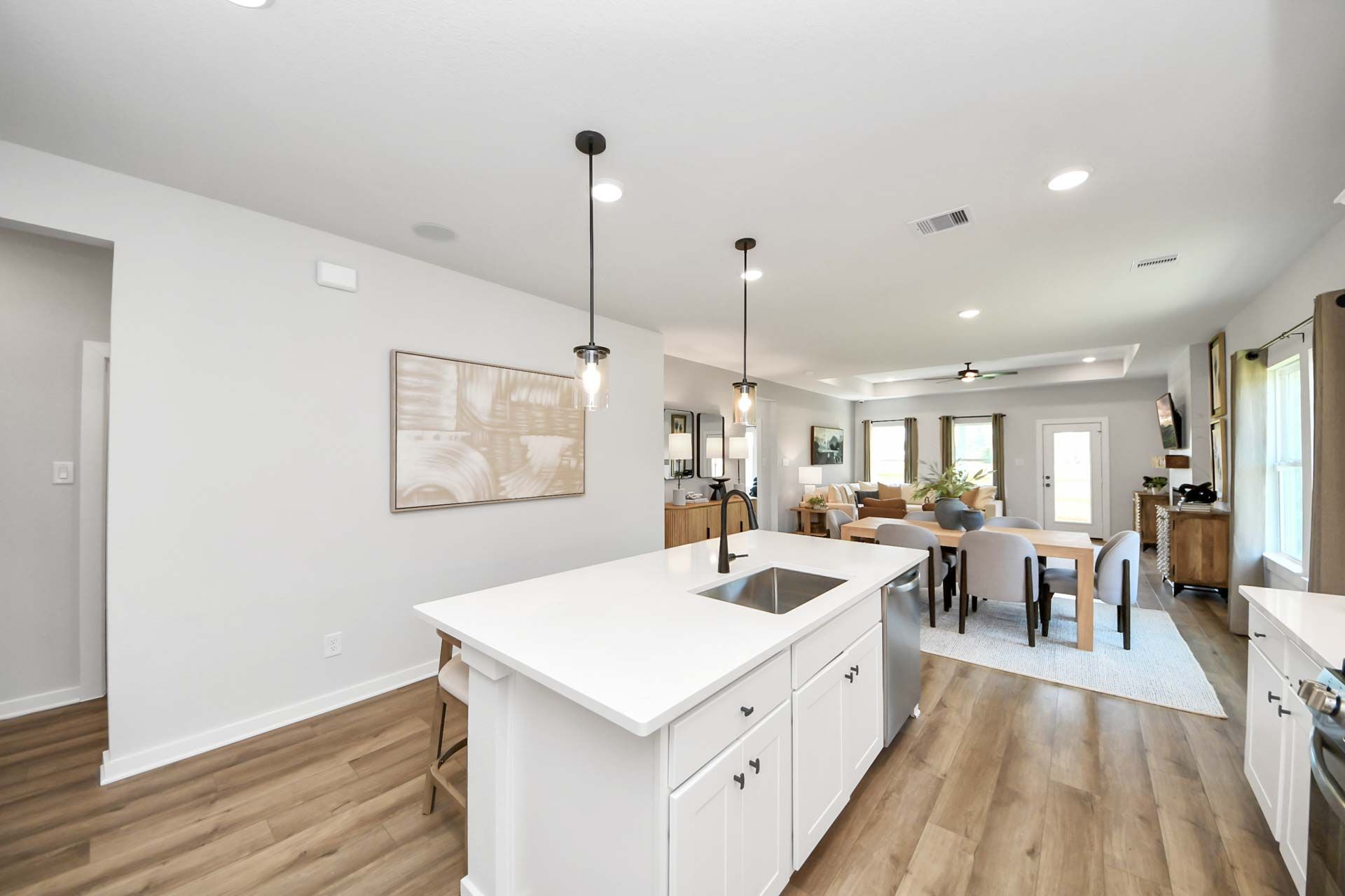Open-concept kitchen and dining area at Enclave at Newport in Crosby, TX, featuring a white island and hardwood floors.