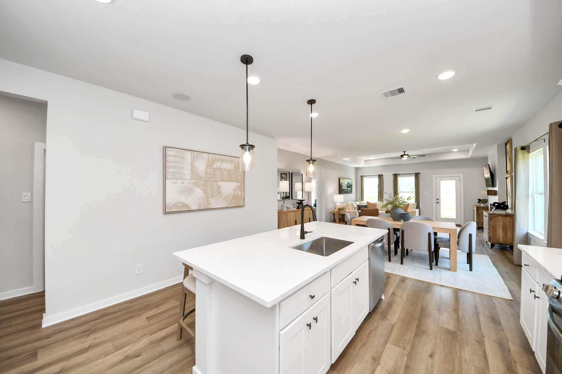 Open-concept kitchen and dining area at Enclave at Newport in Crosby, TX, featuring a white island and hardwood floors.