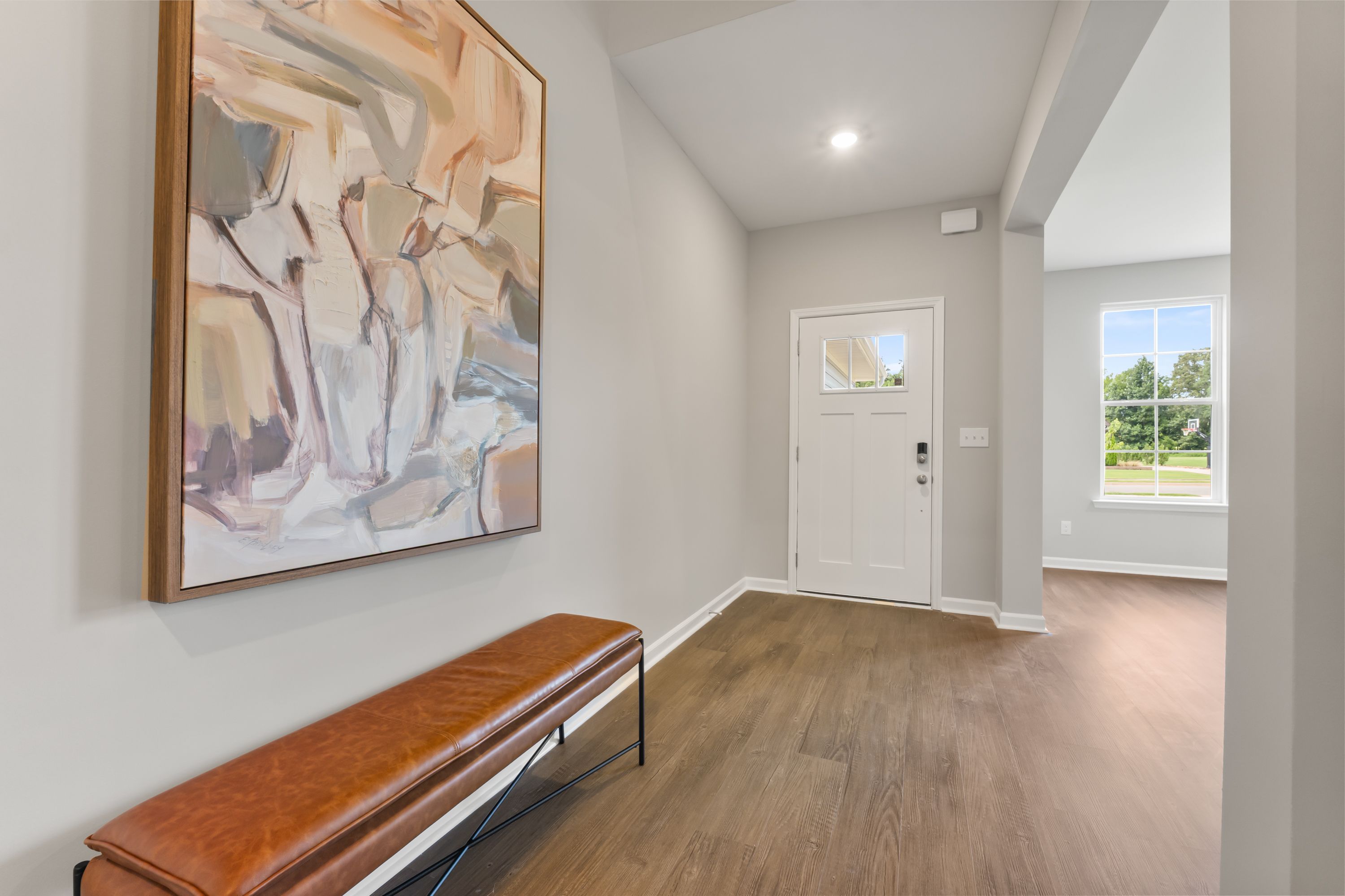 Modern entryway in The Avalon E home featuring abstract orange wall art, leather bench, glass door, and hardwood floors