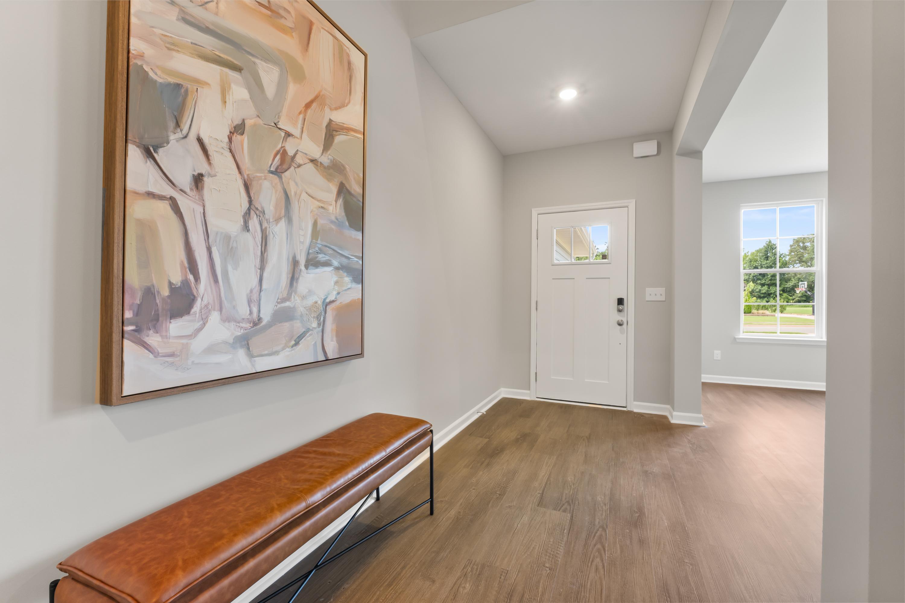 Spacious Avalon D foyer featuring abstract orange painting, leather bench, hardwood floors, and glass-paneled white door
