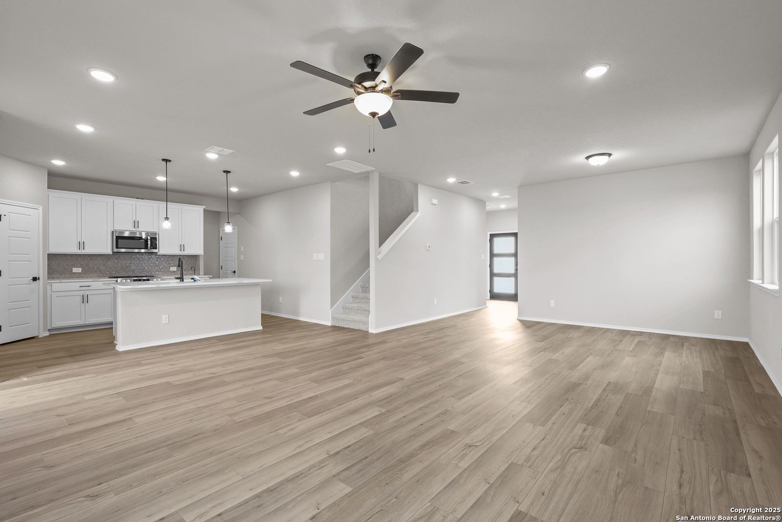 Open-concept kitchen and living area with white cabinets, island, hardwood floors, and ceiling fan in Davidson Homes The Murray J, San Antonio