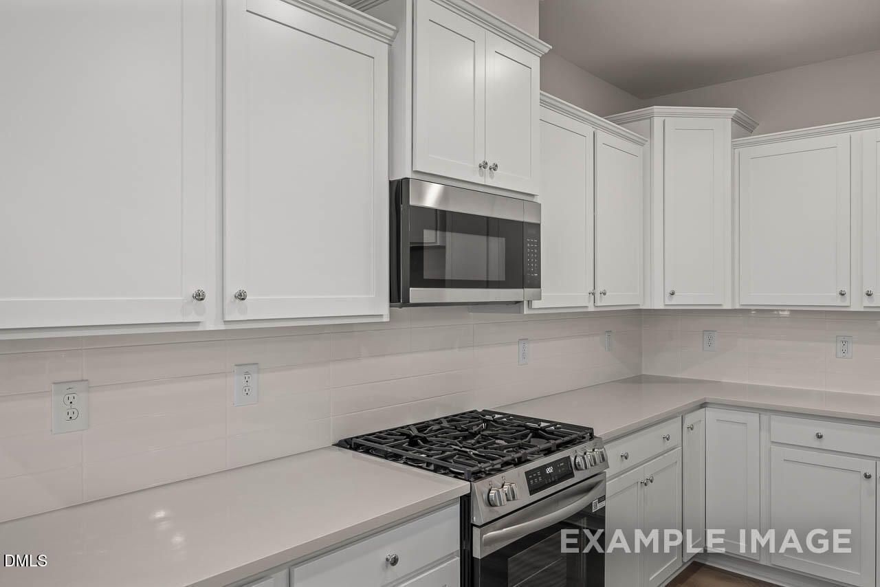 Modern white shaker cabinets, stainless steel microwave and oven, quartz countertops in The Graham kitchen by Davidson Homes, Fuquay-Varina, NC