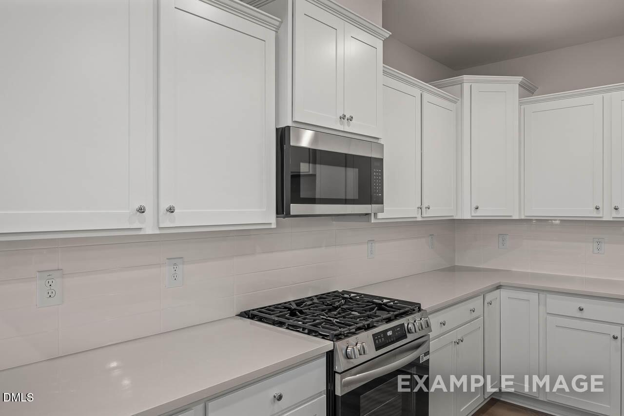 Modern white shaker cabinets, stainless steel microwave and oven, quartz countertops in The Graham kitchen by Davidson Homes, Fuquay-Varina, NC