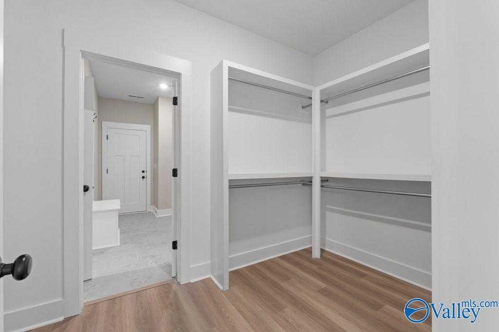 Spacious white walk-in closet with built-in shelves and hanging rods, hardwood floors, in Evermore Homes The Oxford master suite, Owens Cross Roads, AL
