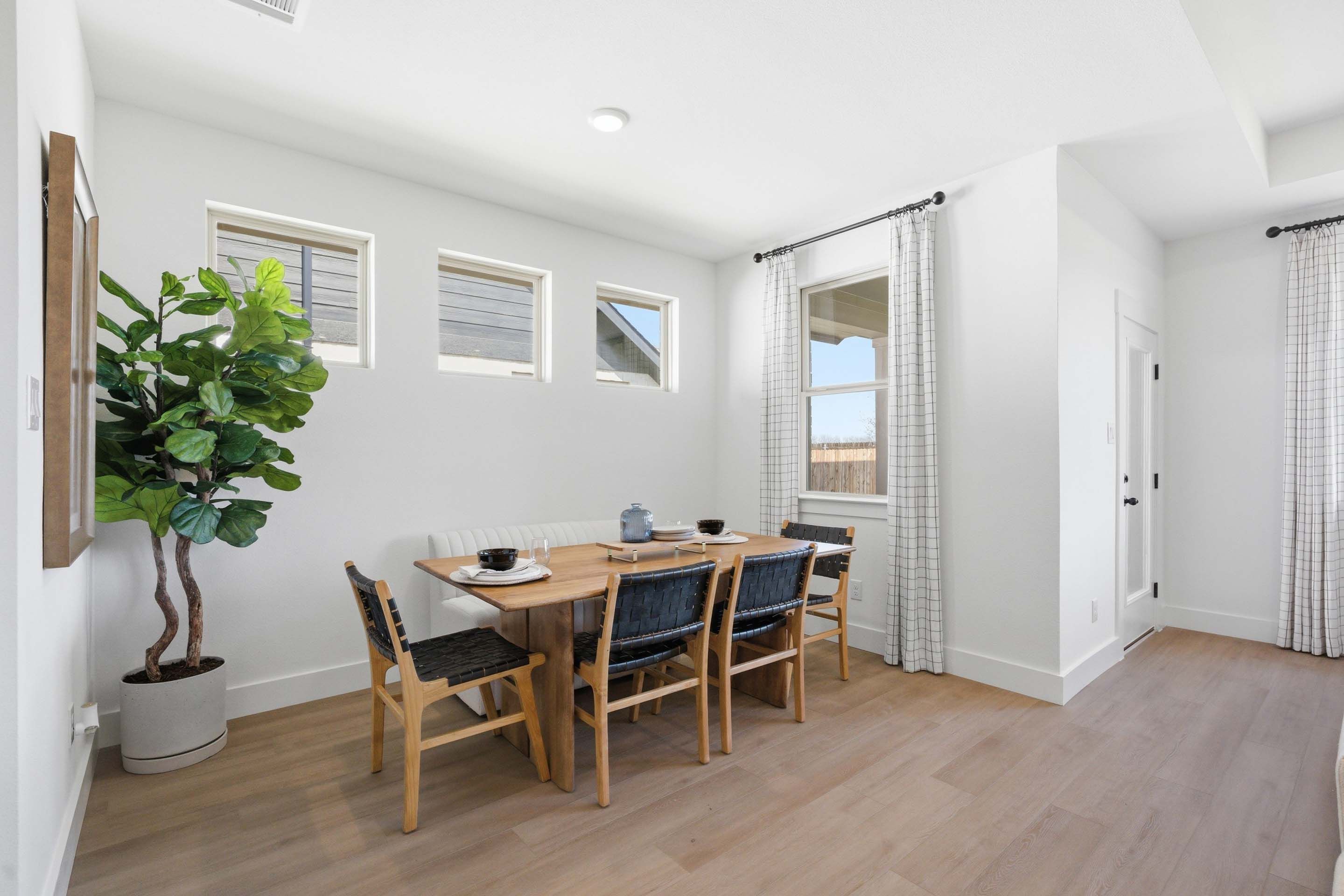 Bright dining area in The Laurel featuring a modern wooden table, woven chairs, and built-in bench seating.