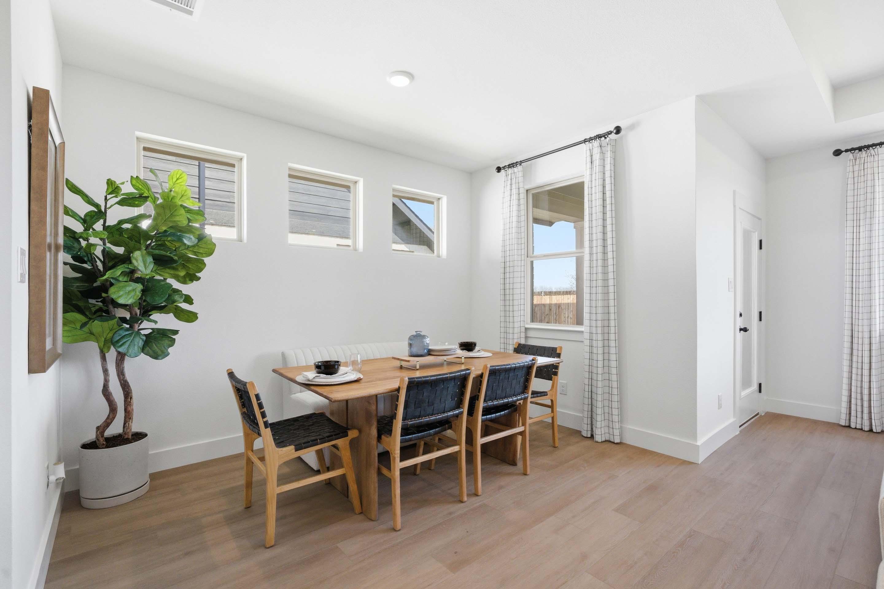 Bright dining area in The Laurel featuring a modern wooden table, woven chairs, and built-in bench seating.
