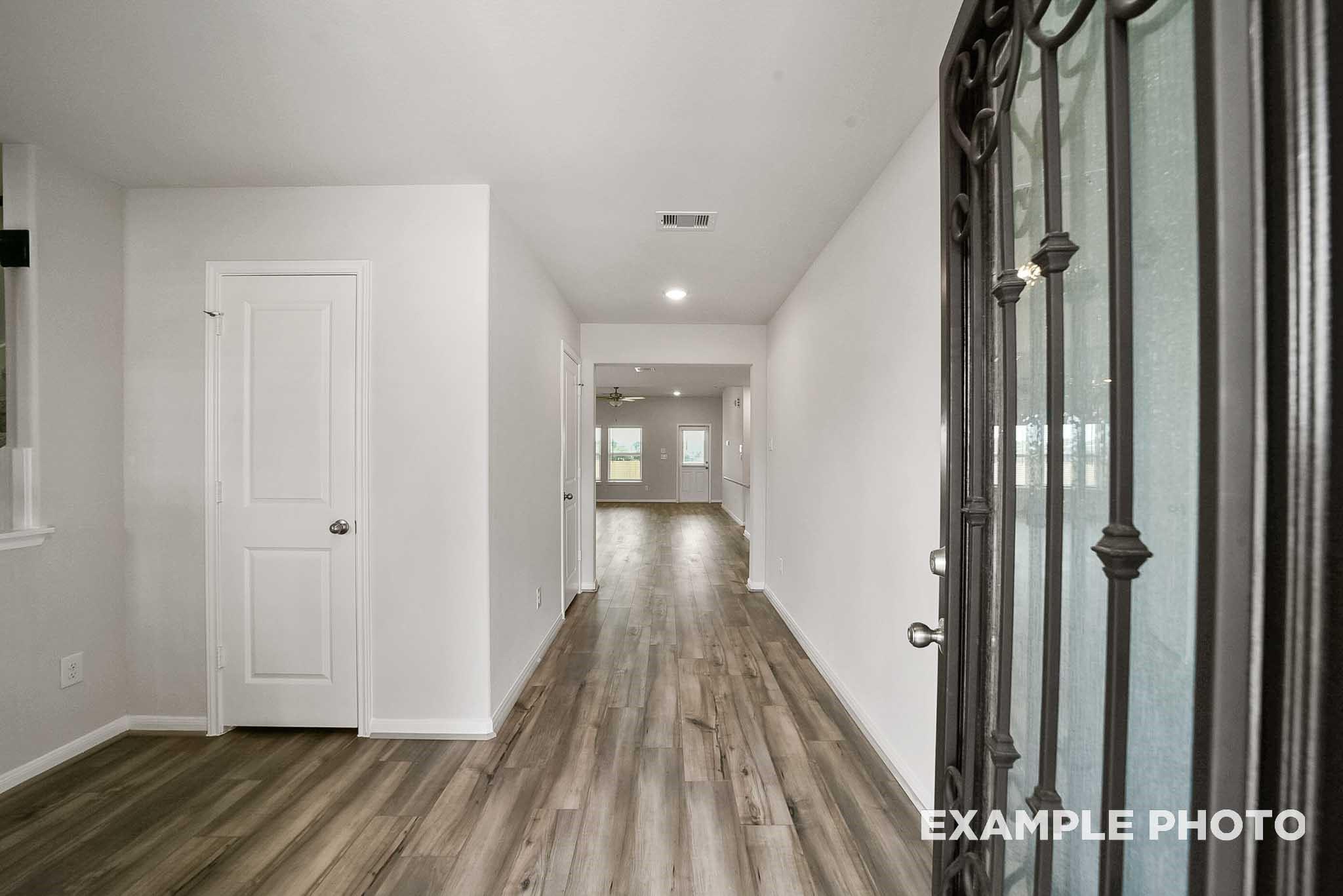 Spacious hallway with hardwood floors, white walls, and wrought iron entry door in 4-bedroom Tierra B home, Emberly, Beasley, Texas