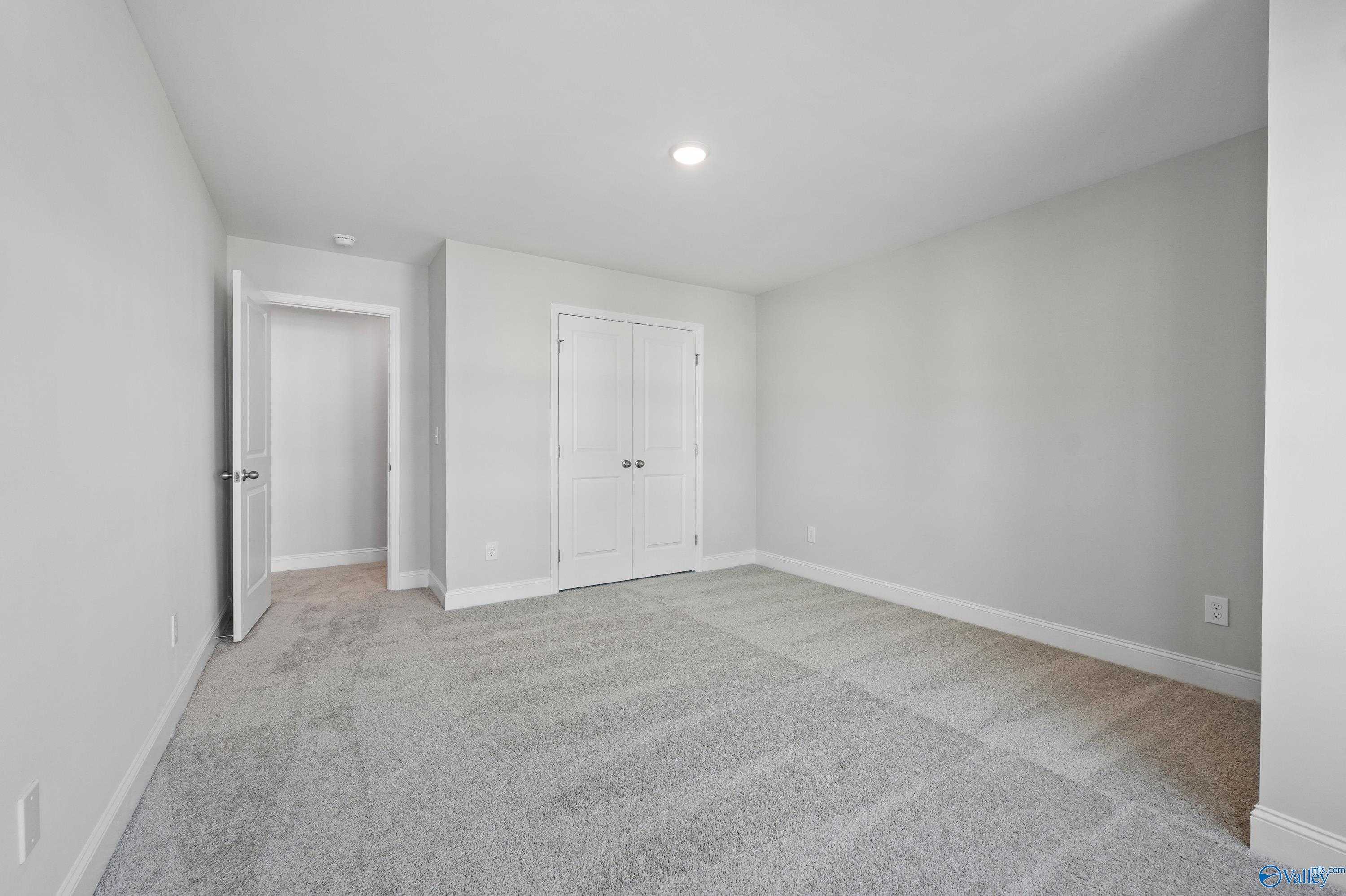 Spacious empty bedroom with double-door closet, gray walls, and carpet flooring in Davidson Homes The Camden, Huntsville AL