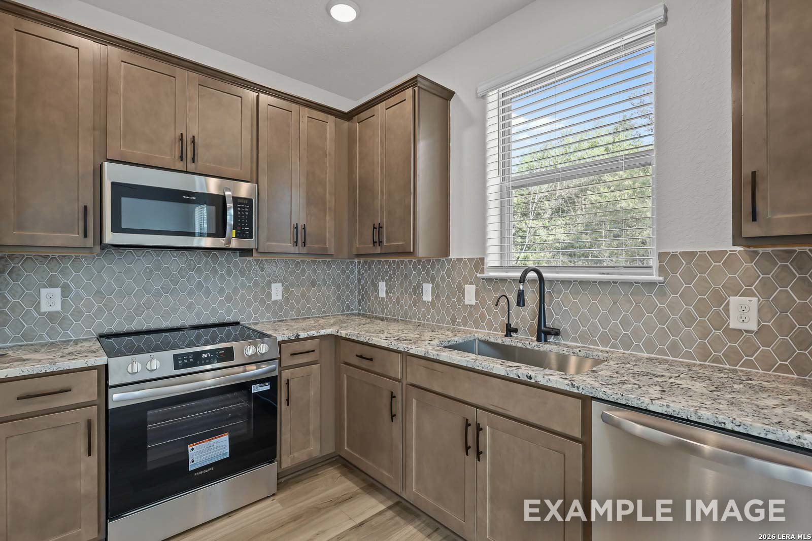 Modern kitchen with granite countertops, tile backsplash, and stainless appliances in The Florence D at Cedar Heights.