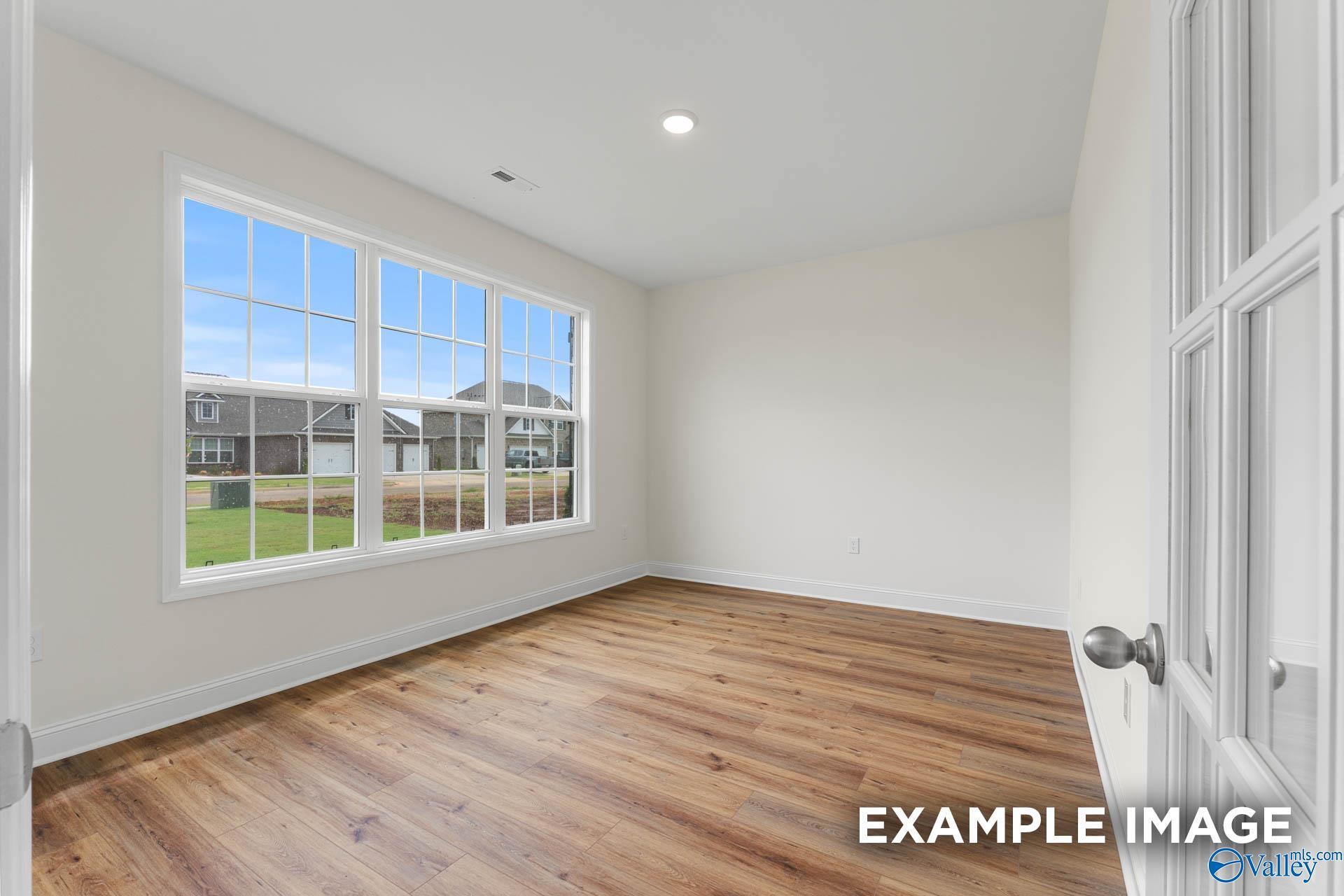 Bright empty bedroom with hardwood floors, large windows, and yard view in Davidson Homes The Emory, Toney, Alabama