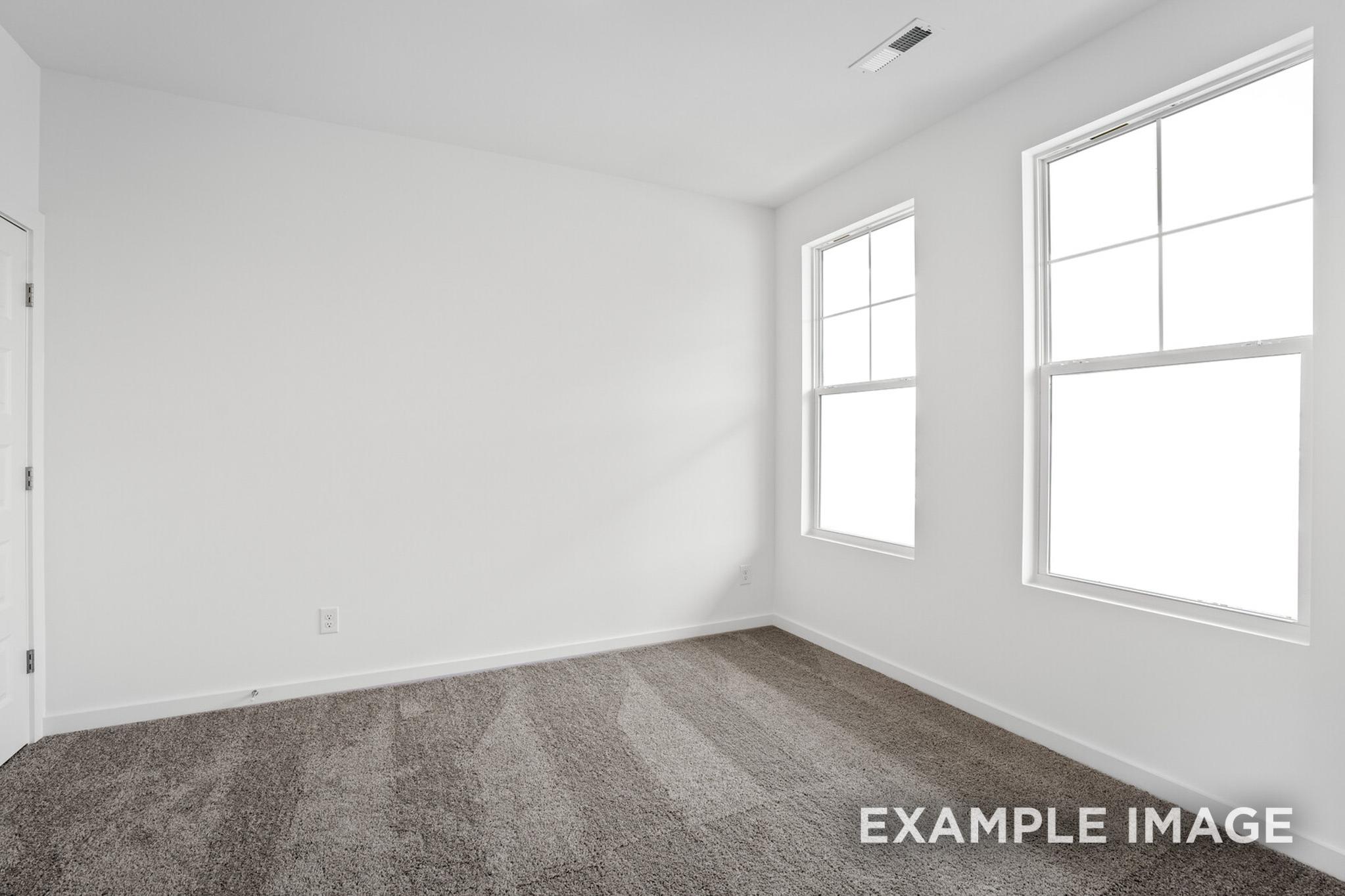 Spacious empty bedroom in The Logan C home with white walls, large double-hung windows, and gray carpet flooring