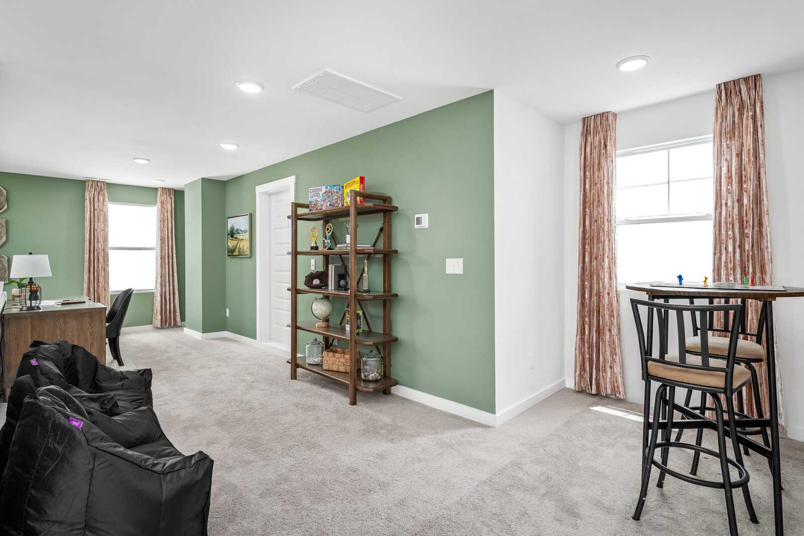 Cozy loft bonus room at Calista Farms in White House TN with sage green wall, bookshelves, desk, bar stools and bean bag seating
