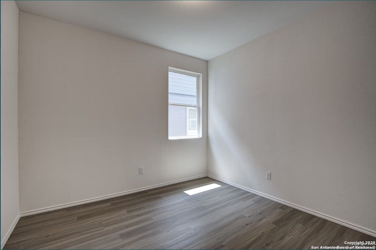 Bright secondary bedroom with luxury vinyl plank floors, beige walls, and sunlit window in The Daphne H, Seguin, Texas