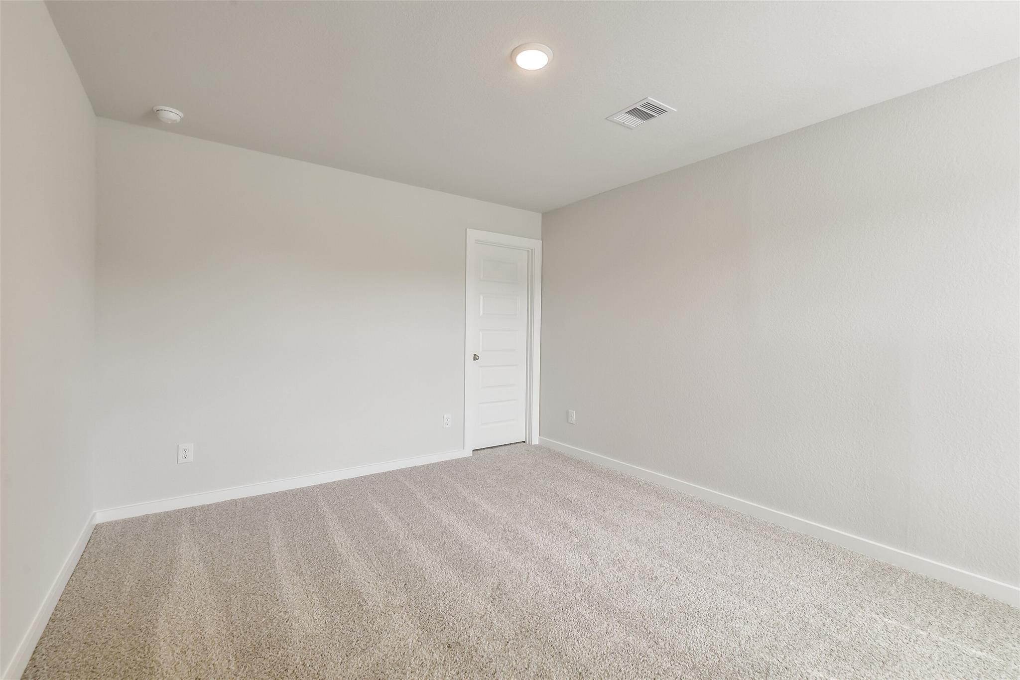 Empty bedroom with light gray walls, white door, beige carpet, and recessed ceiling light in Davidson Homes San Marcos E, Conroe TX