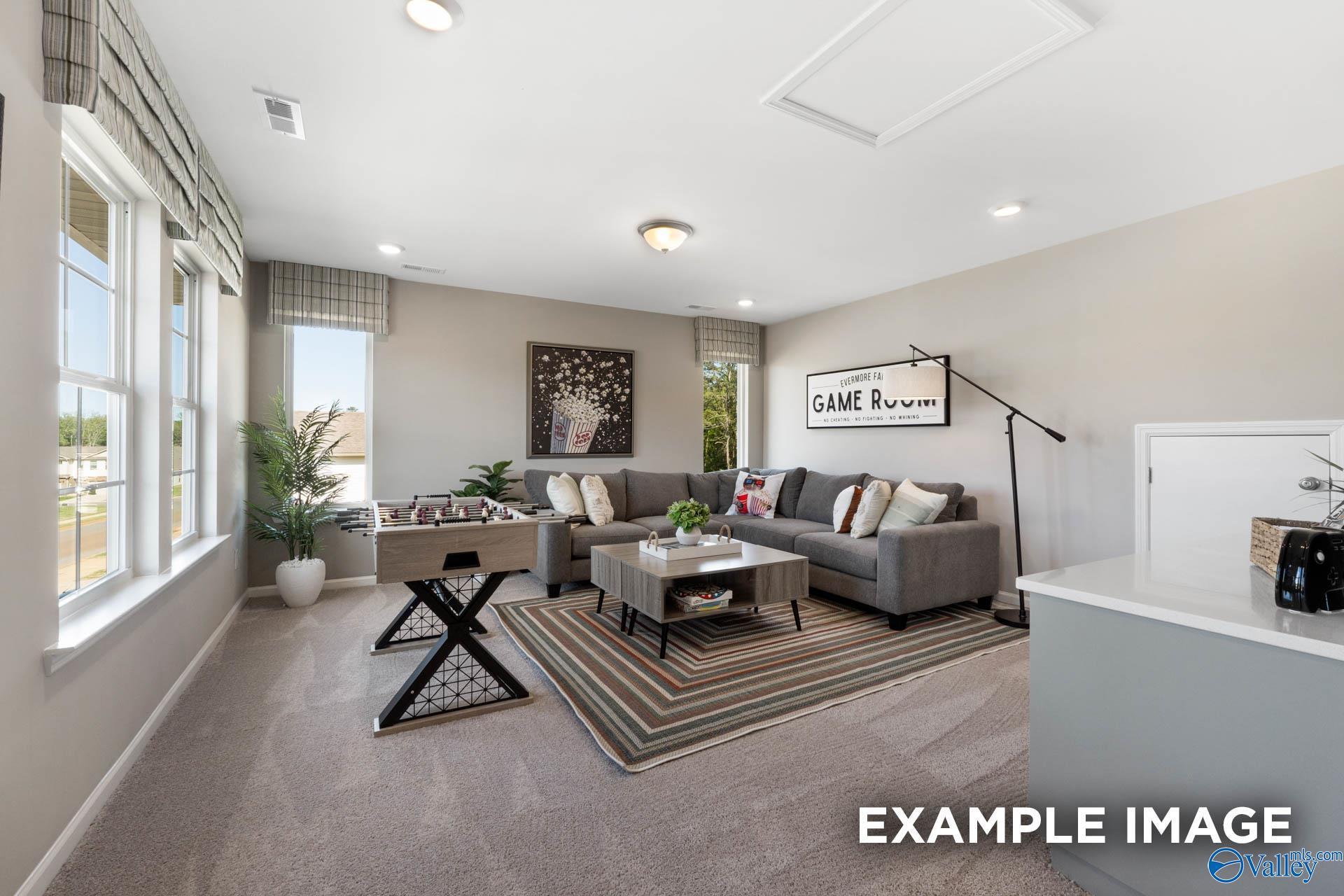 Cozy game room with gray L-shaped sofa, coffee table, plants, and large windows in Davidson Homes The Stella, Madison, Alabama