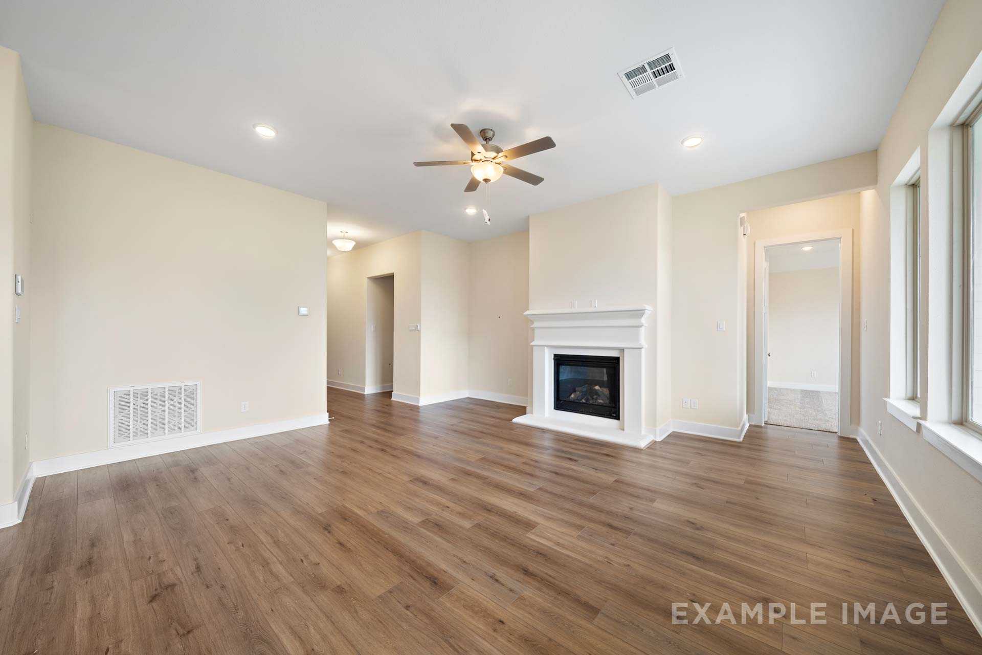 Spacious living room in The Diana C home design with gas fireplace, ceiling fan, hardwood floors, and large windows