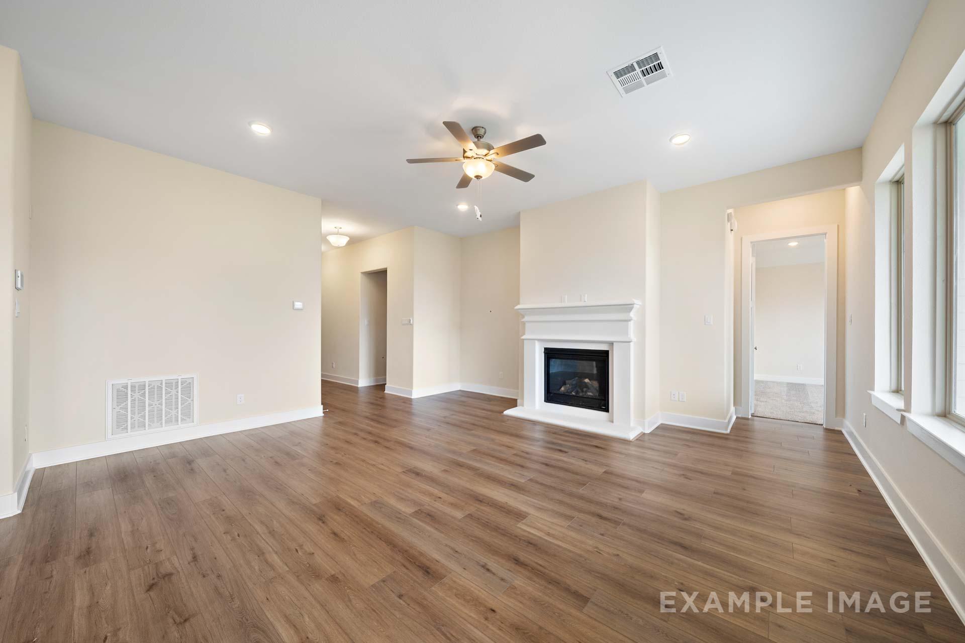 Spacious living room in The Diana C home design with gas fireplace, ceiling fan, hardwood floors, and large windows