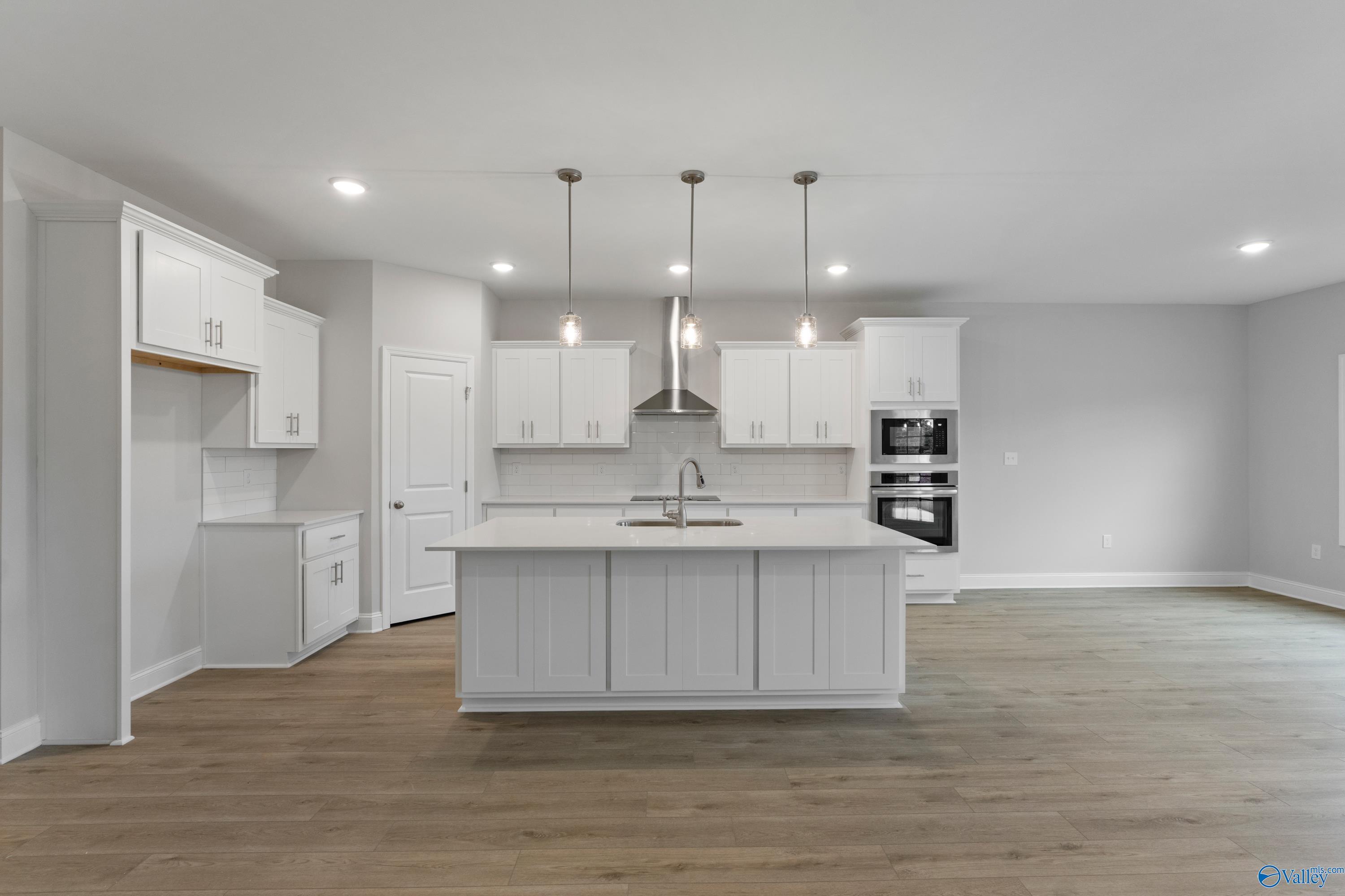 Modern white shaker kitchen with oversized island, farmhouse sink, and pendant lights in Davidson Homes The Rockford B, Toney, AL