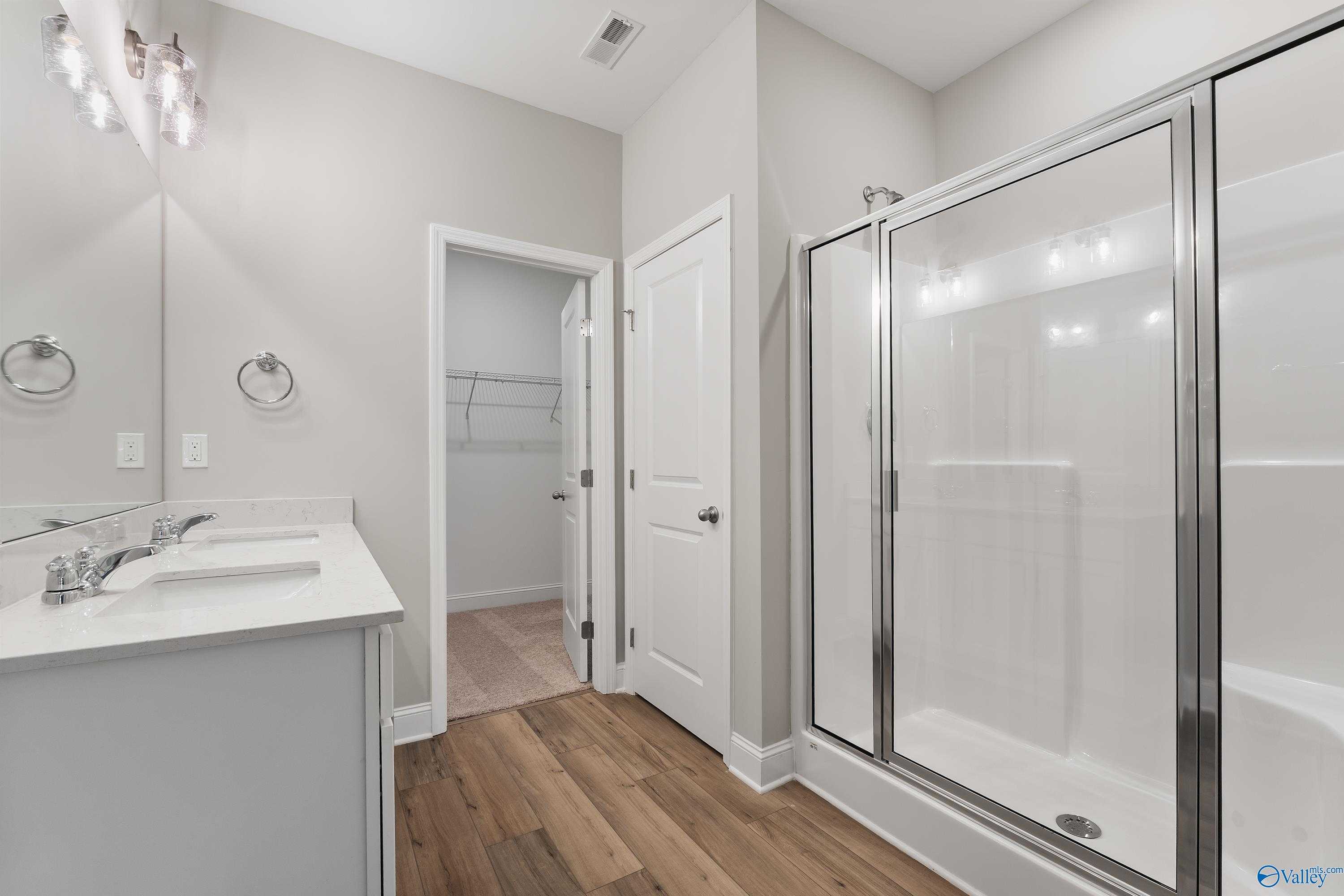Modern master bathroom with white double vanity, frameless glass shower, and wood floors in Davidson Homes The Franklin C, Toney, Alabama
