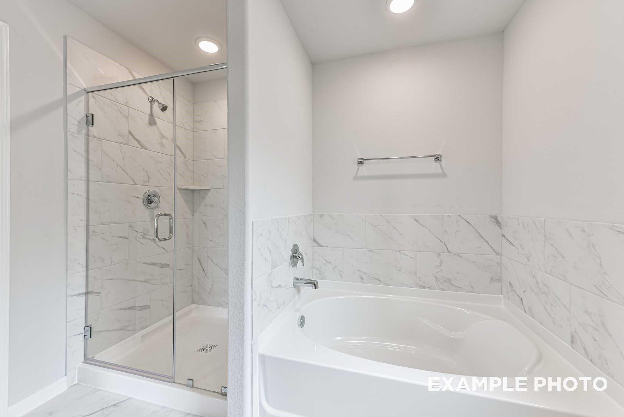 Modern bathroom with marble-tiled walk-in shower and soaking tub in The Costa A floor plan at Emberly, Beasley, Texas.