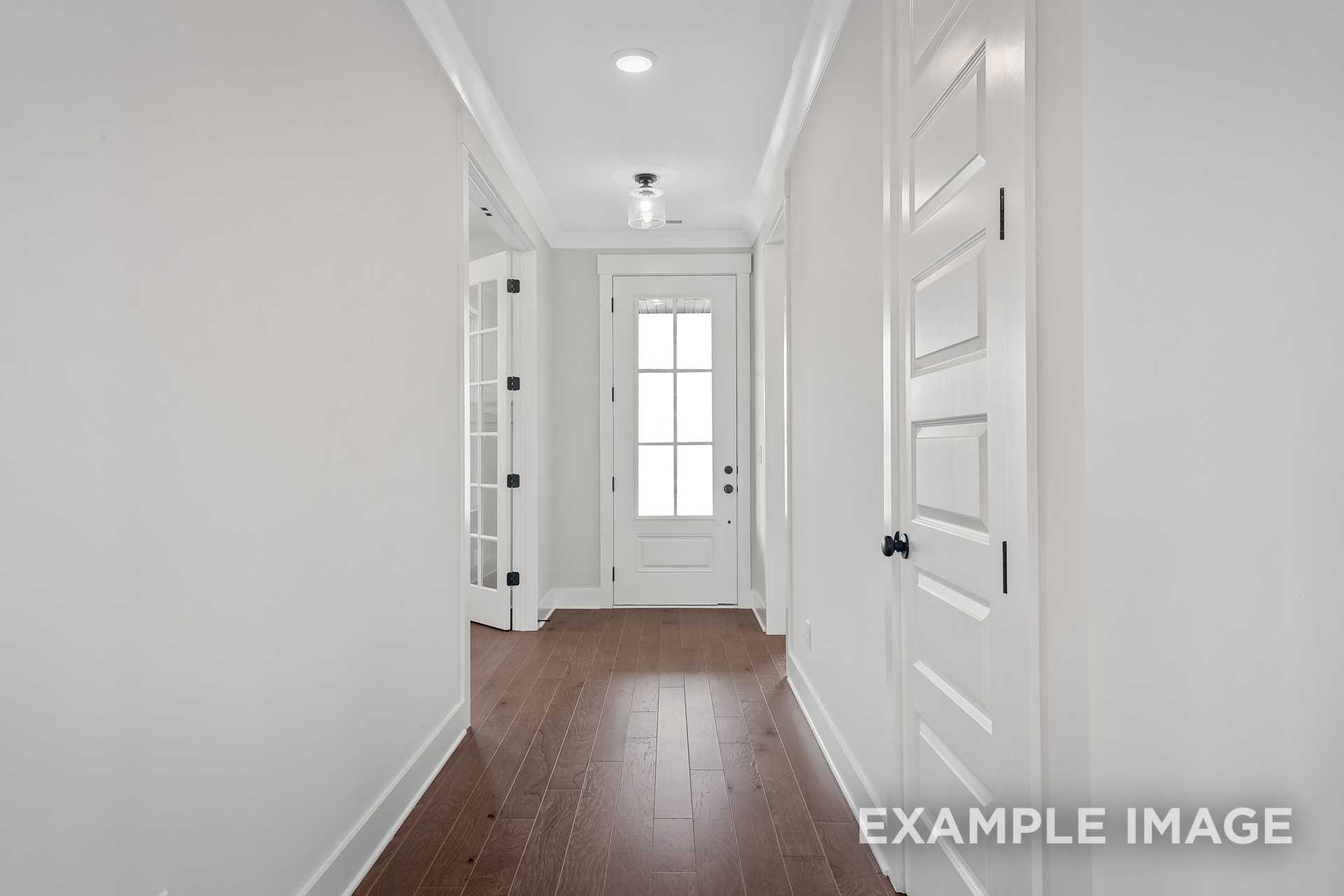 Spacious hallway in The Hathaway with hardwood floors, white paneled doors, and glass transom window, Davidson Homes Murfreesboro