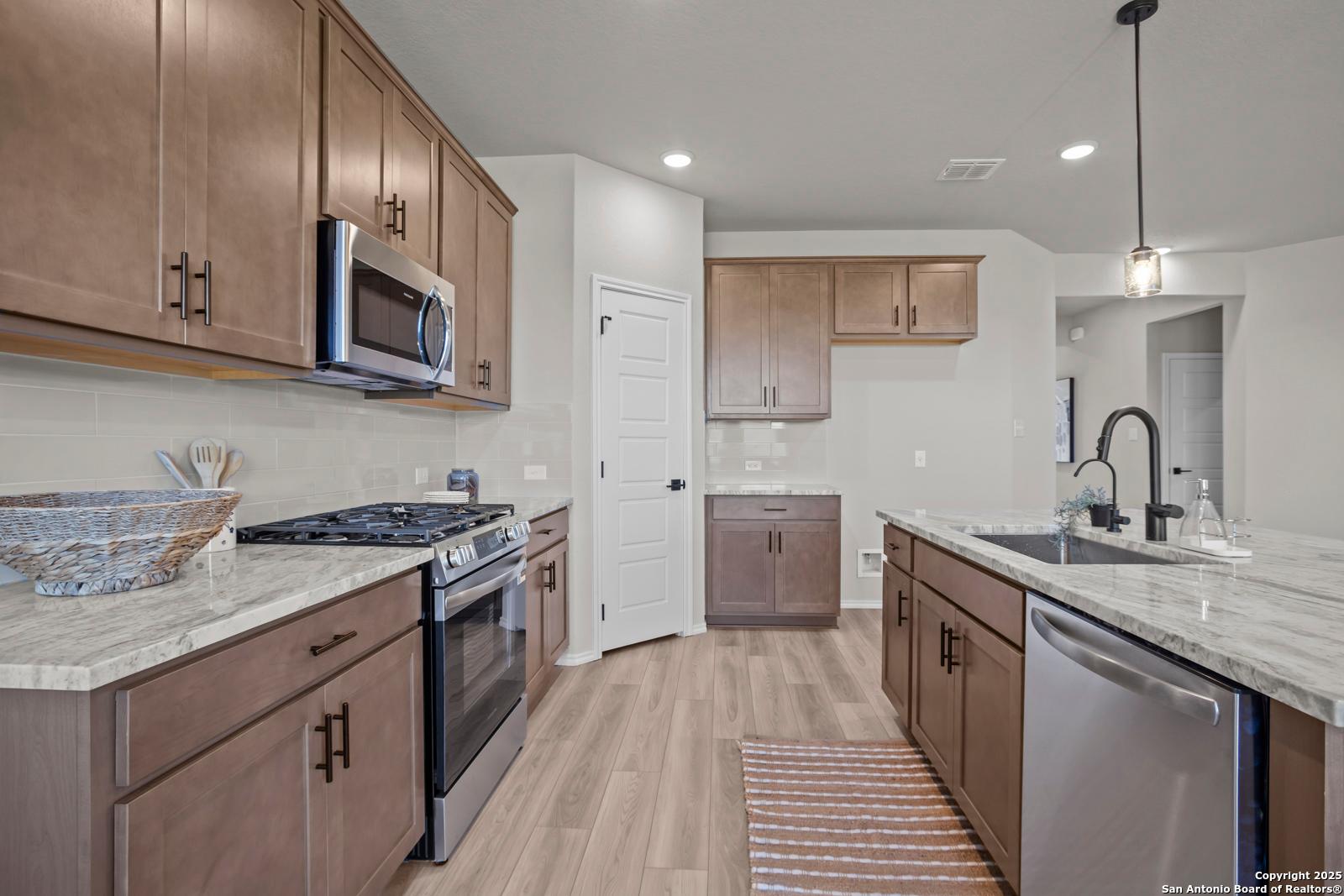 Open-concept kitchen with warm shaker cabinets, white quartz counters, stainless appliances in The Asheville H by Davidson Homes, Converse TX