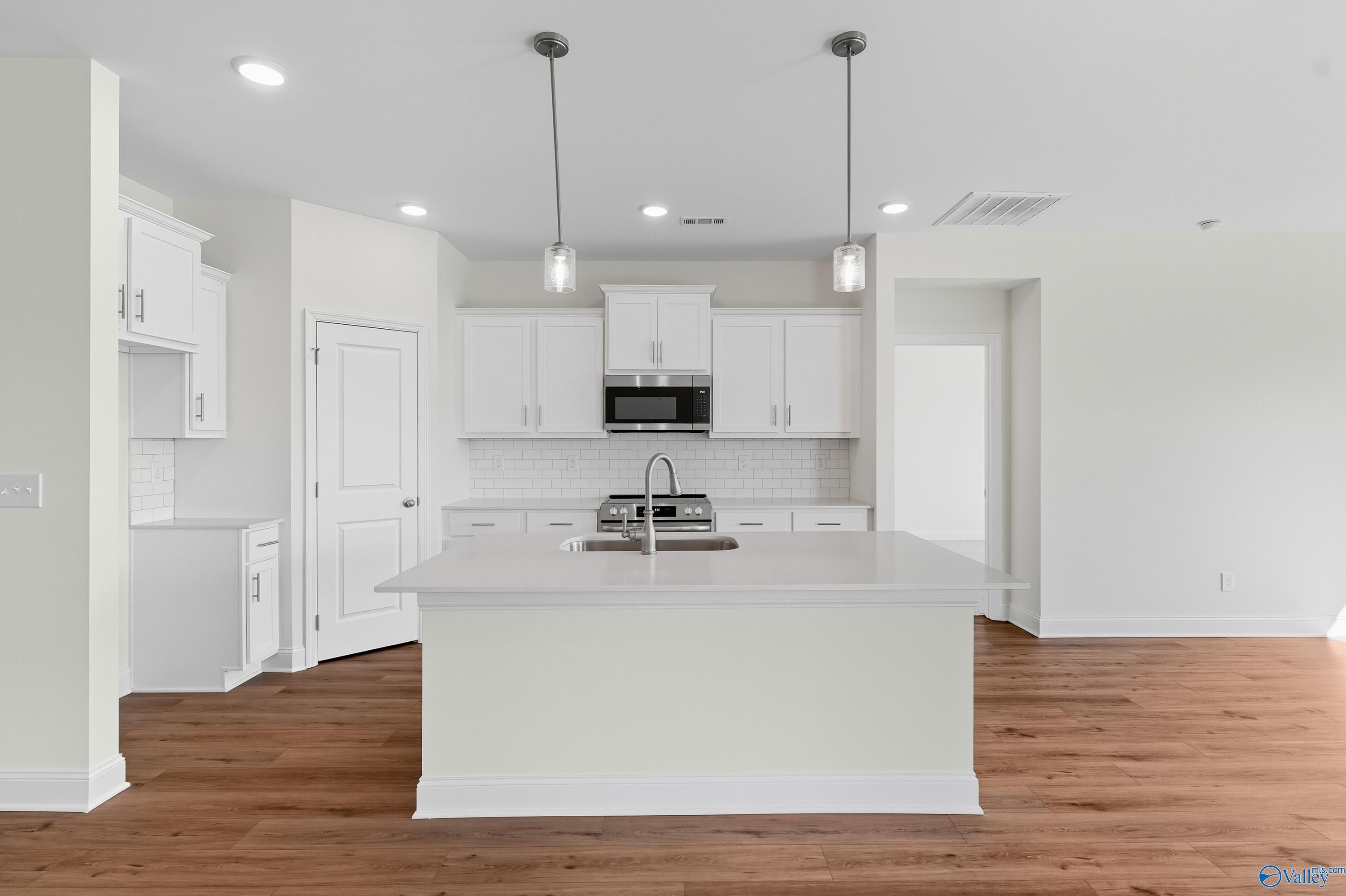 Bright white kitchen with central island, stainless appliances, pendant lights in Davidson Homes The Everett, Meridianville, Alabama