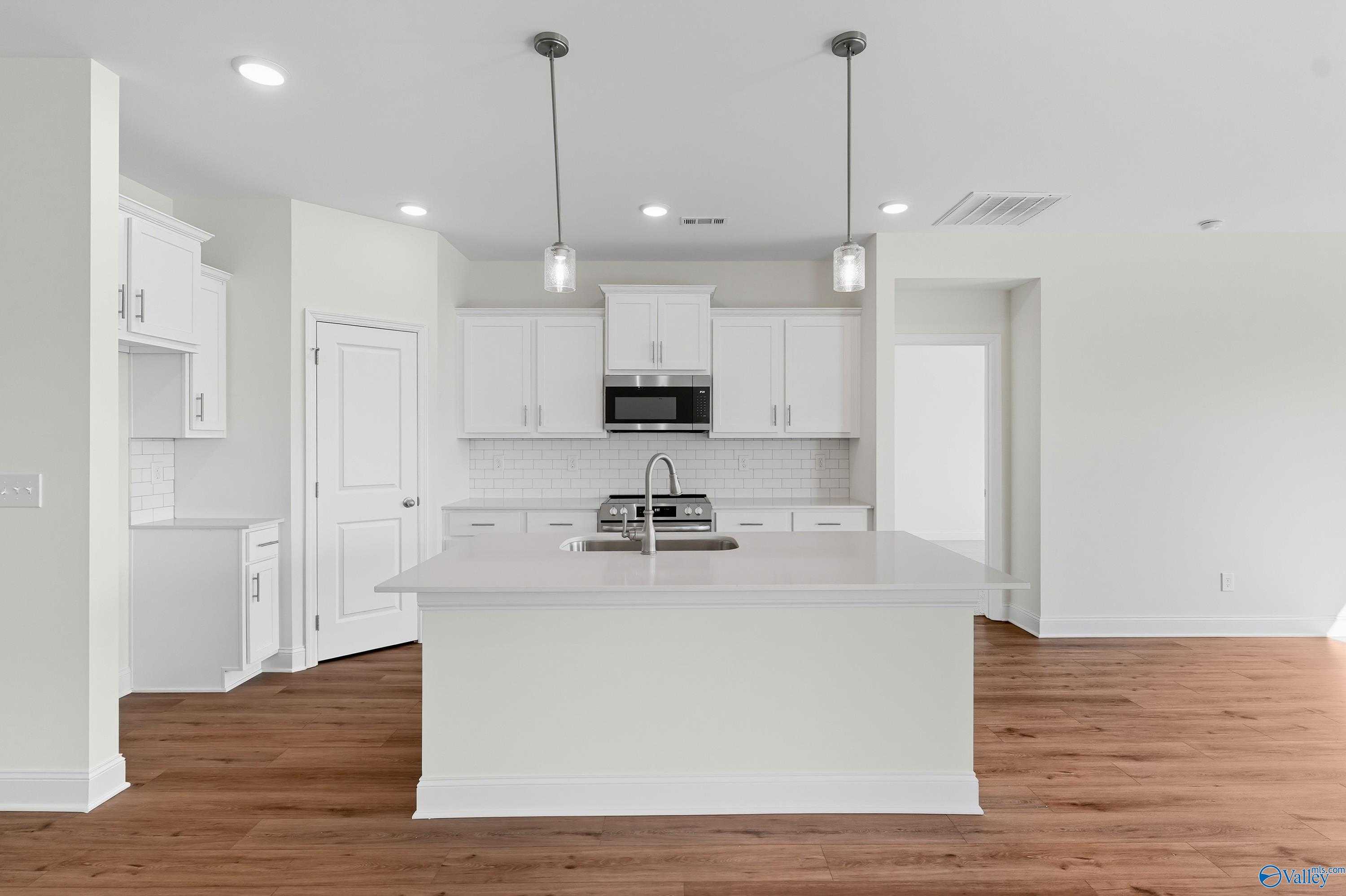 Modern white kitchen with island sink, stainless appliances, pendant lights, and hardwood floors in Davidson Homes The Everett, Meridianville, Alabama