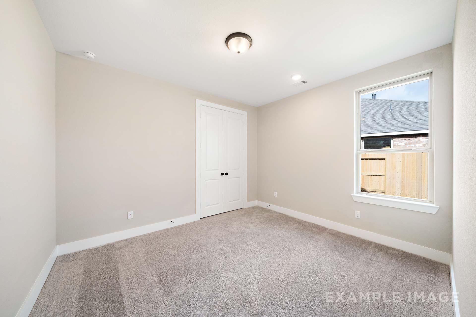 Spacious secondary bedroom in The Elizabeth A Davidson Homes design, beige walls, carpeted floor, large window overlooking backyard