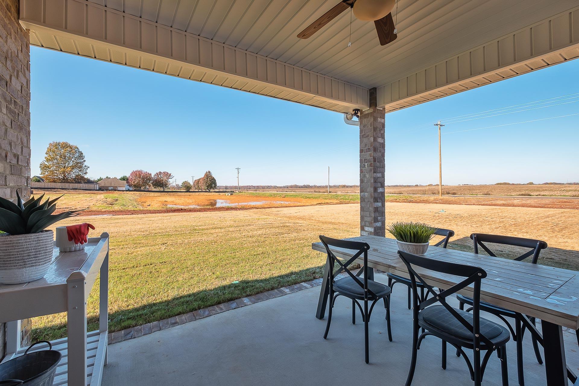 Spacious covered patio at Newby Chapel in Athens Alabama with wooden dining table, black chairs, potted plants, and scenic field views