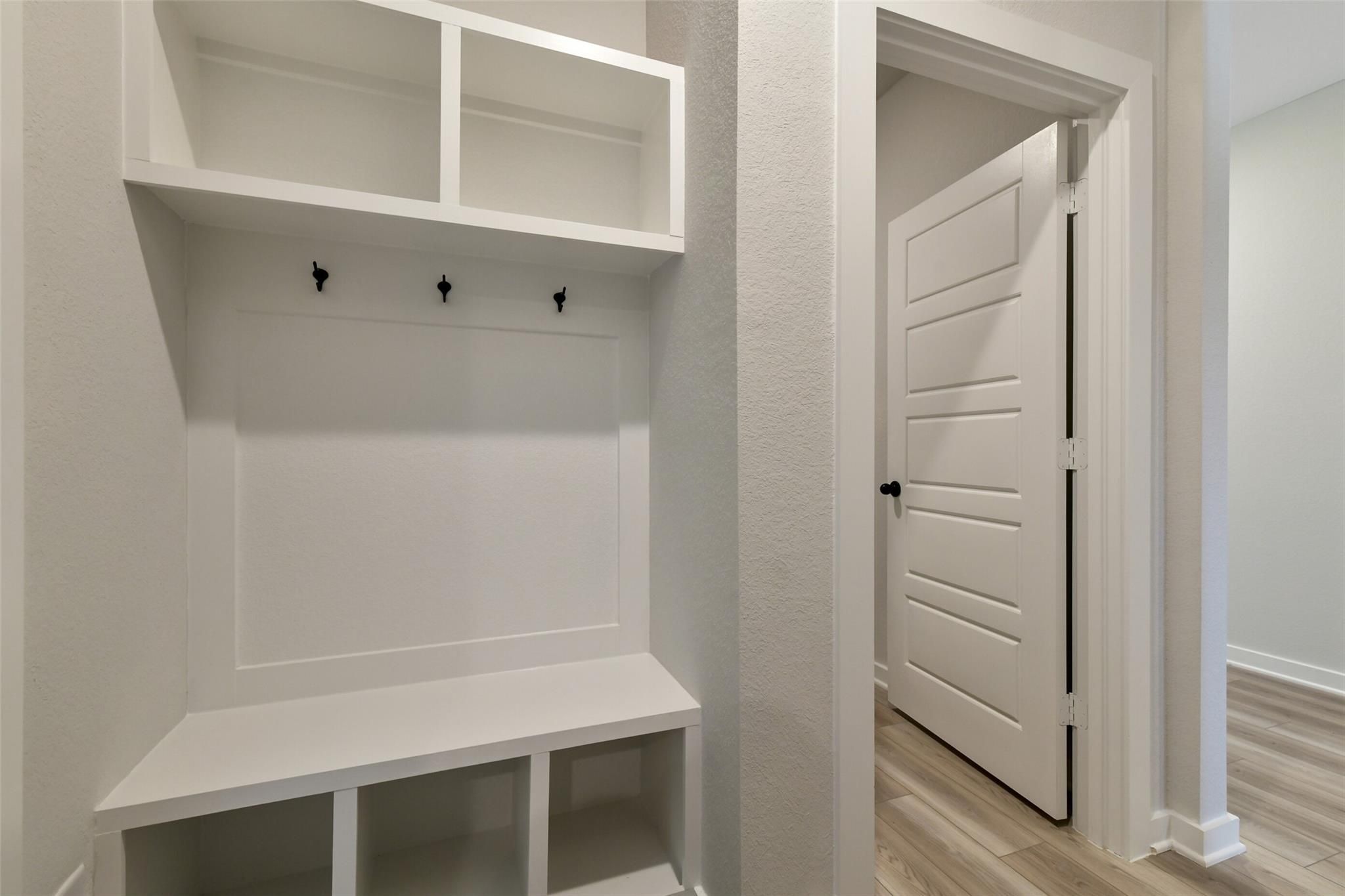 Modern white mudroom with built-in bench, coat hooks, and open shelves in The Daphne H 4-bedroom home, Sundance Cove, Crosby, Texas