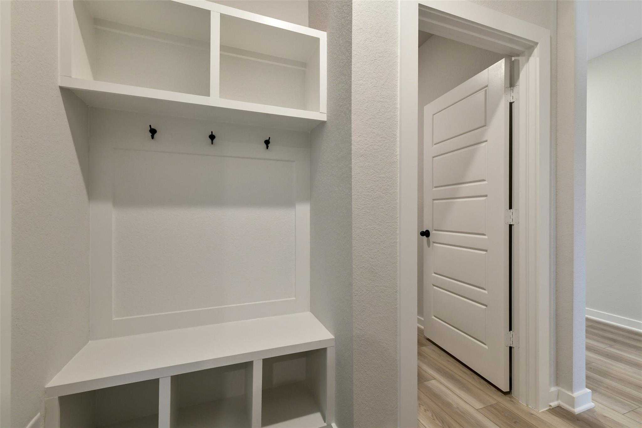 Modern white mudroom with built-in bench, coat hooks, and open shelves in The Daphne H 4-bedroom home, Sundance Cove, Crosby, Texas