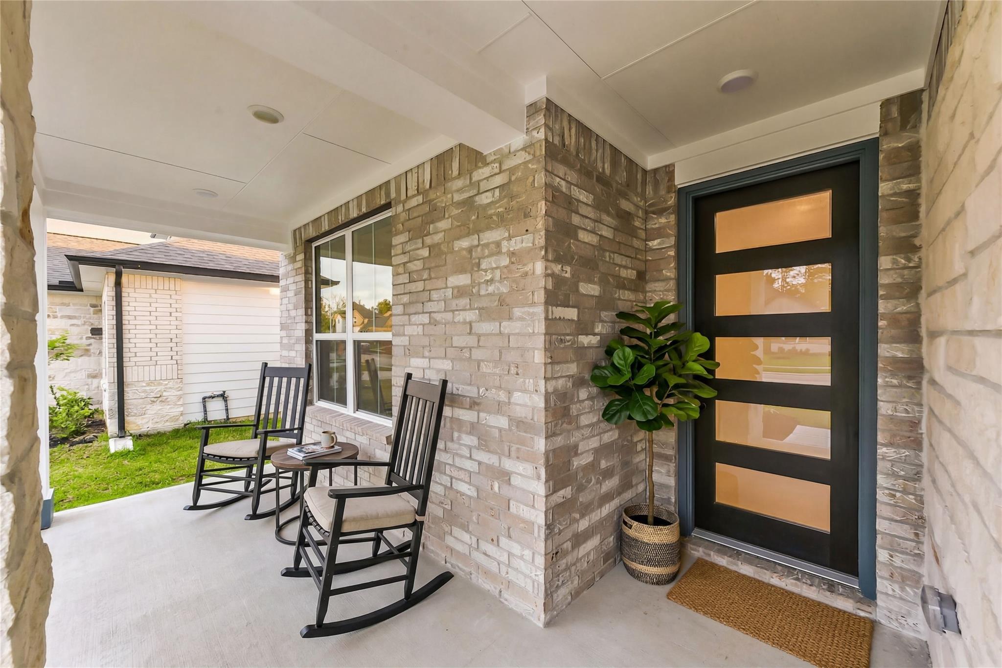 Covered front porch with black rocking chairs, potted fiddle leaf fig, and modern entry door in Davidson Homes Sequoia C, Crosby Texas